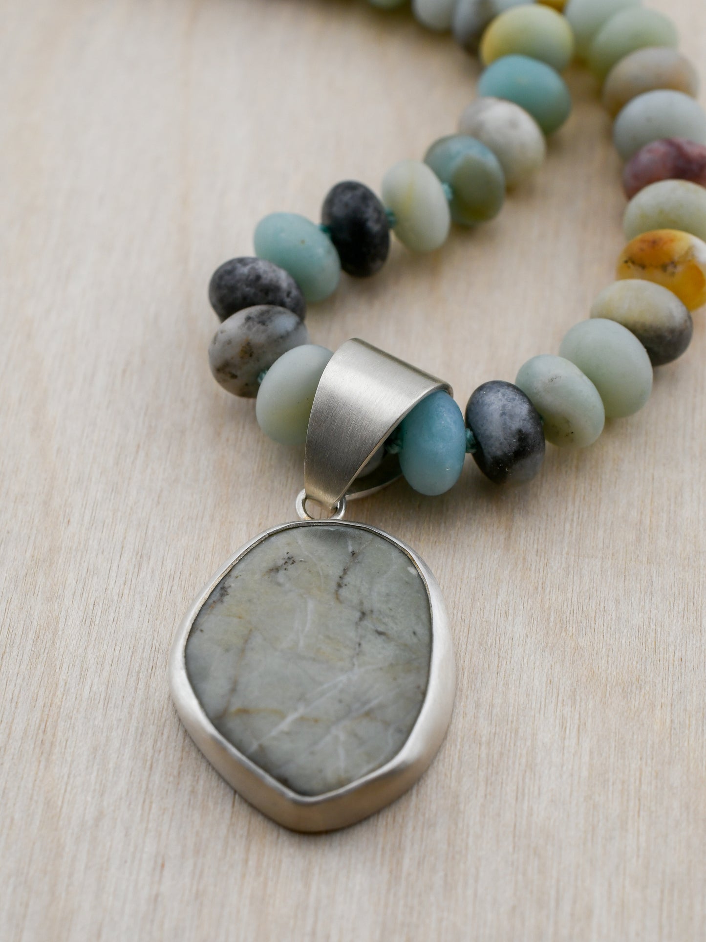 Necklace with multicolored beads and a large stone pendant on a light wooden surface