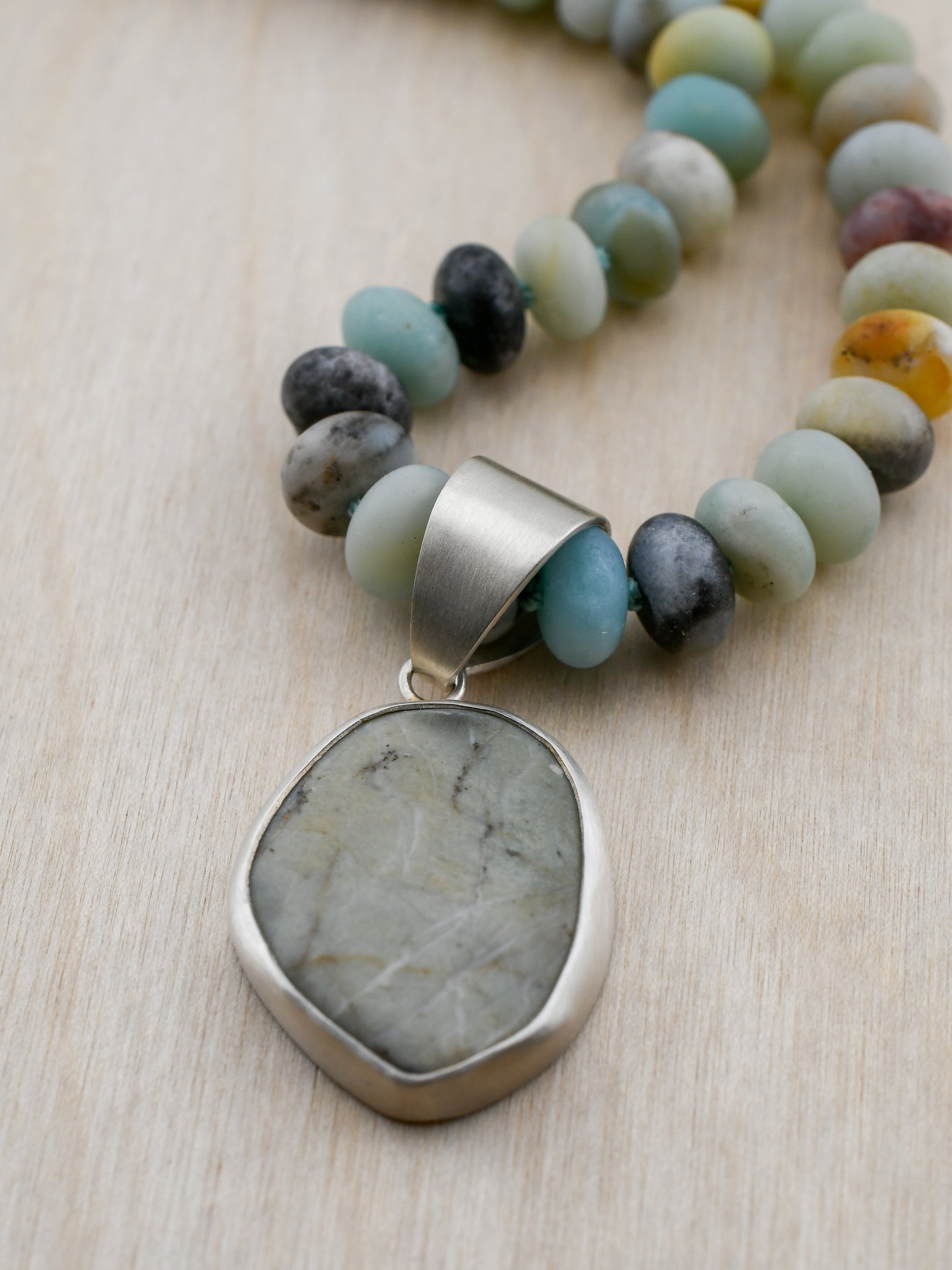 Necklace with multicolored beads and a large stone pendant on a light wooden surface