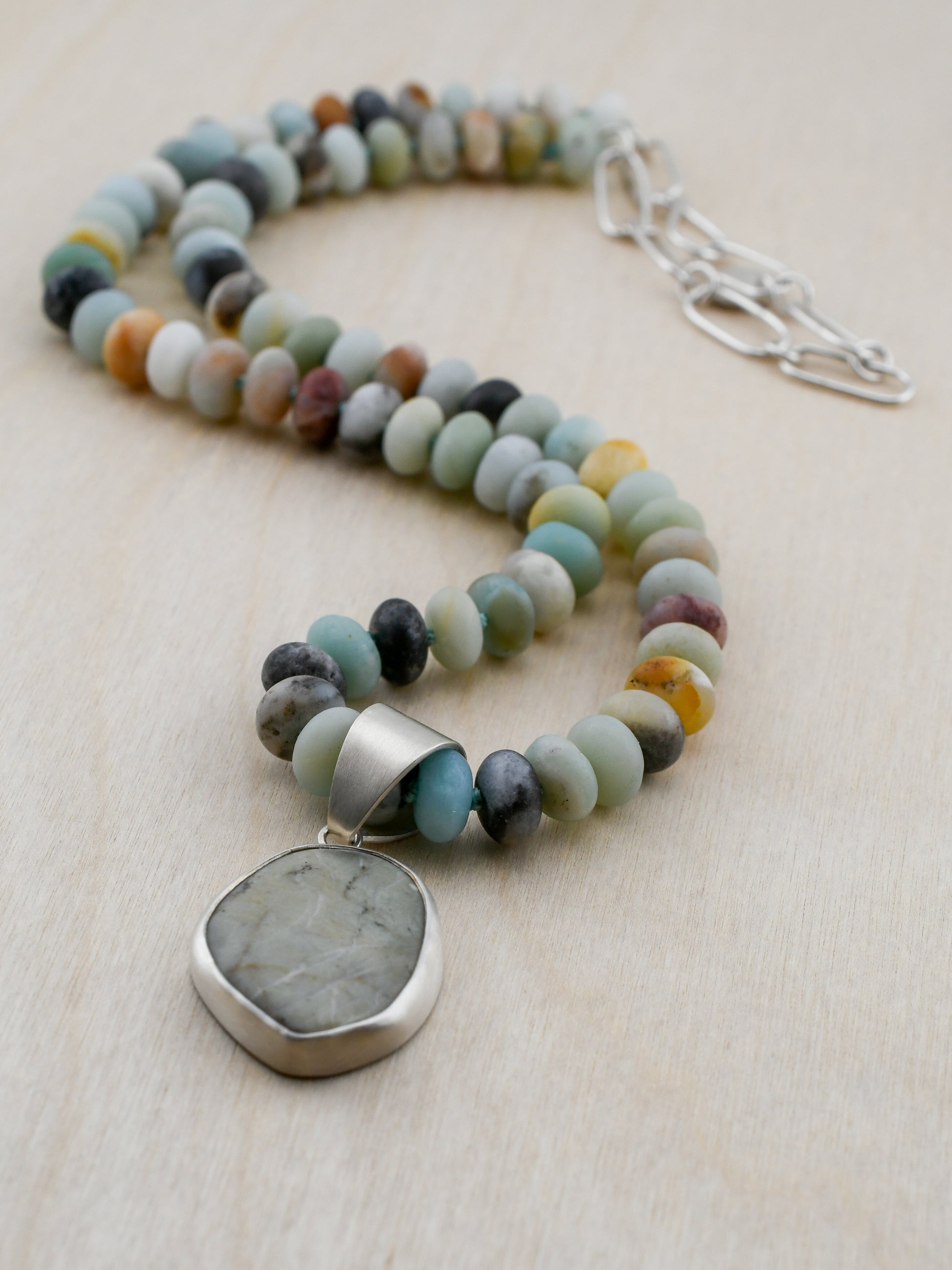 Necklace with multicolored beads and a large stone pendant on a light background