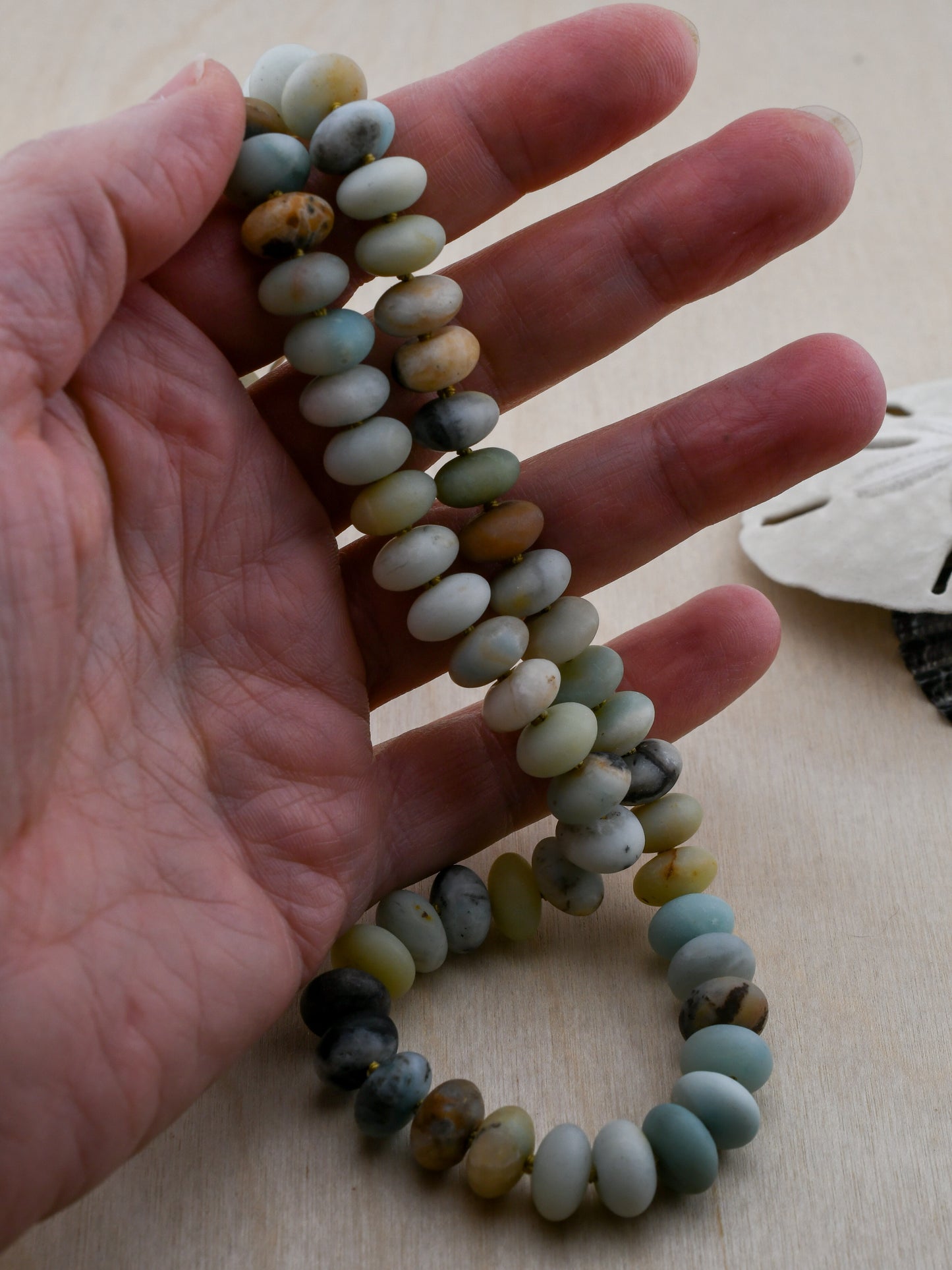 Hand holding a beaded necklace with a neutral background