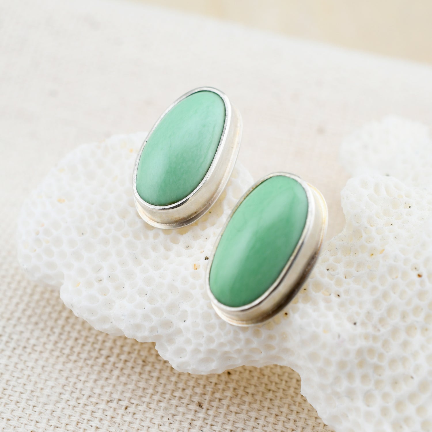 oval mint green variscite and silver stud earrings on white coral with a textured background