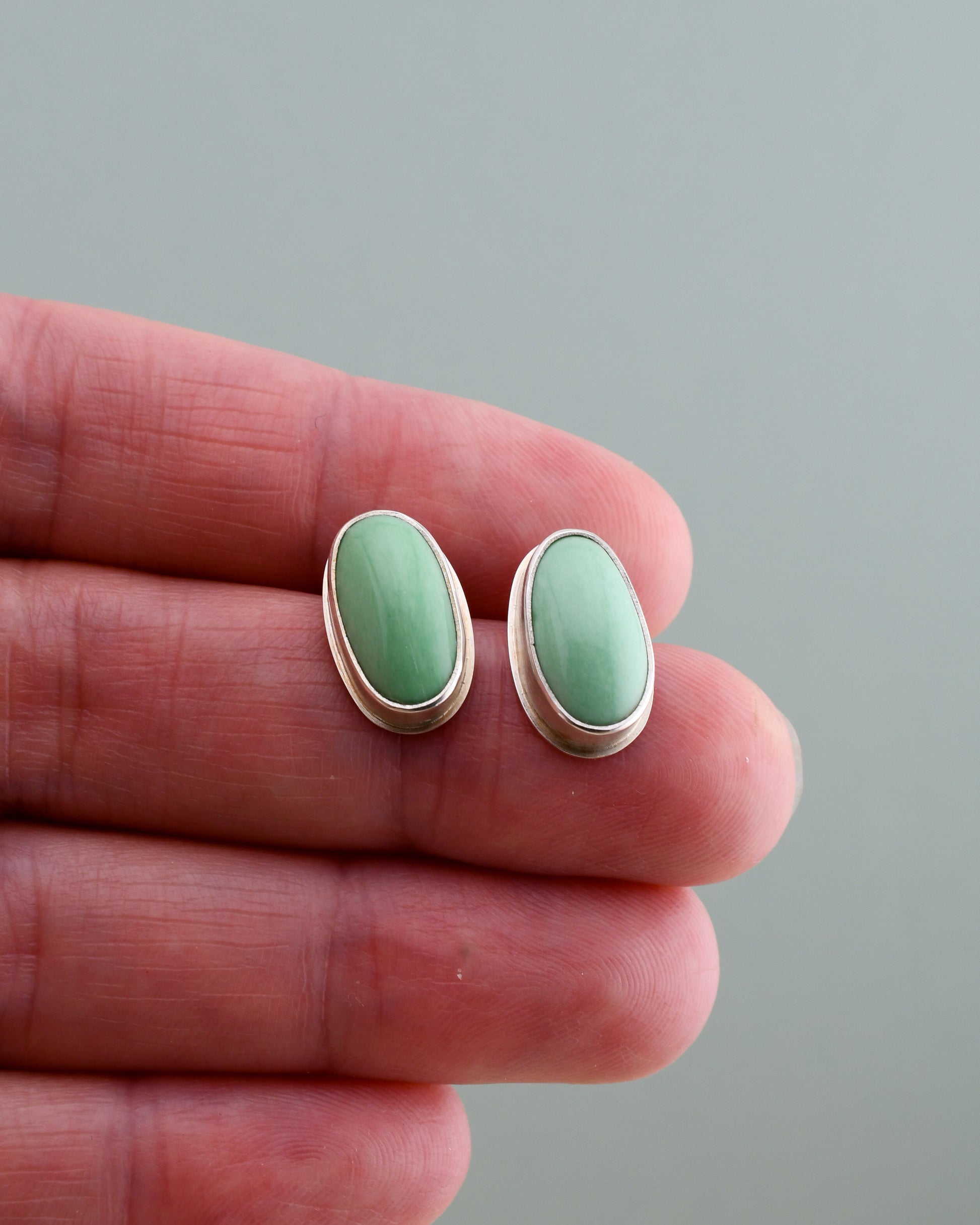 silver and variscite stud earrings held in a hand on a neutral background