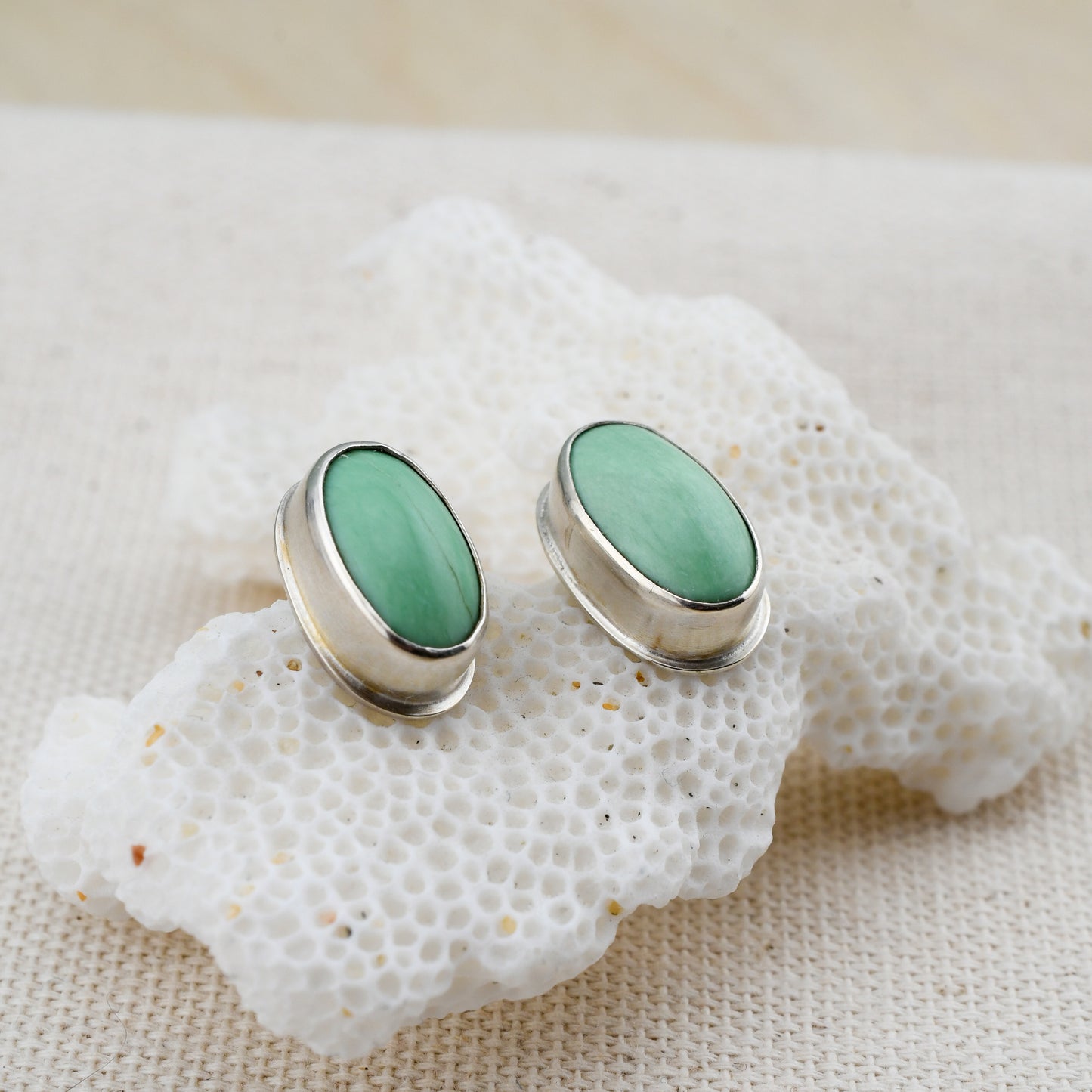 oval green variscite and silver studs displayed on white coral