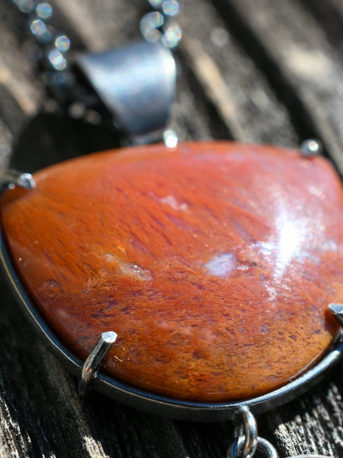 Red and orange stone pendant with metal chain on a wooden surface
