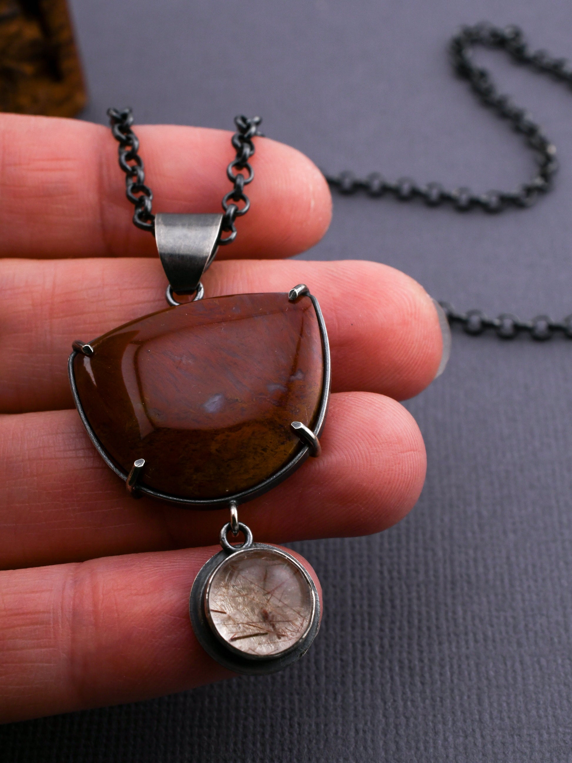 Close-up of a hand holding a pendant with a red stone and silver chain.