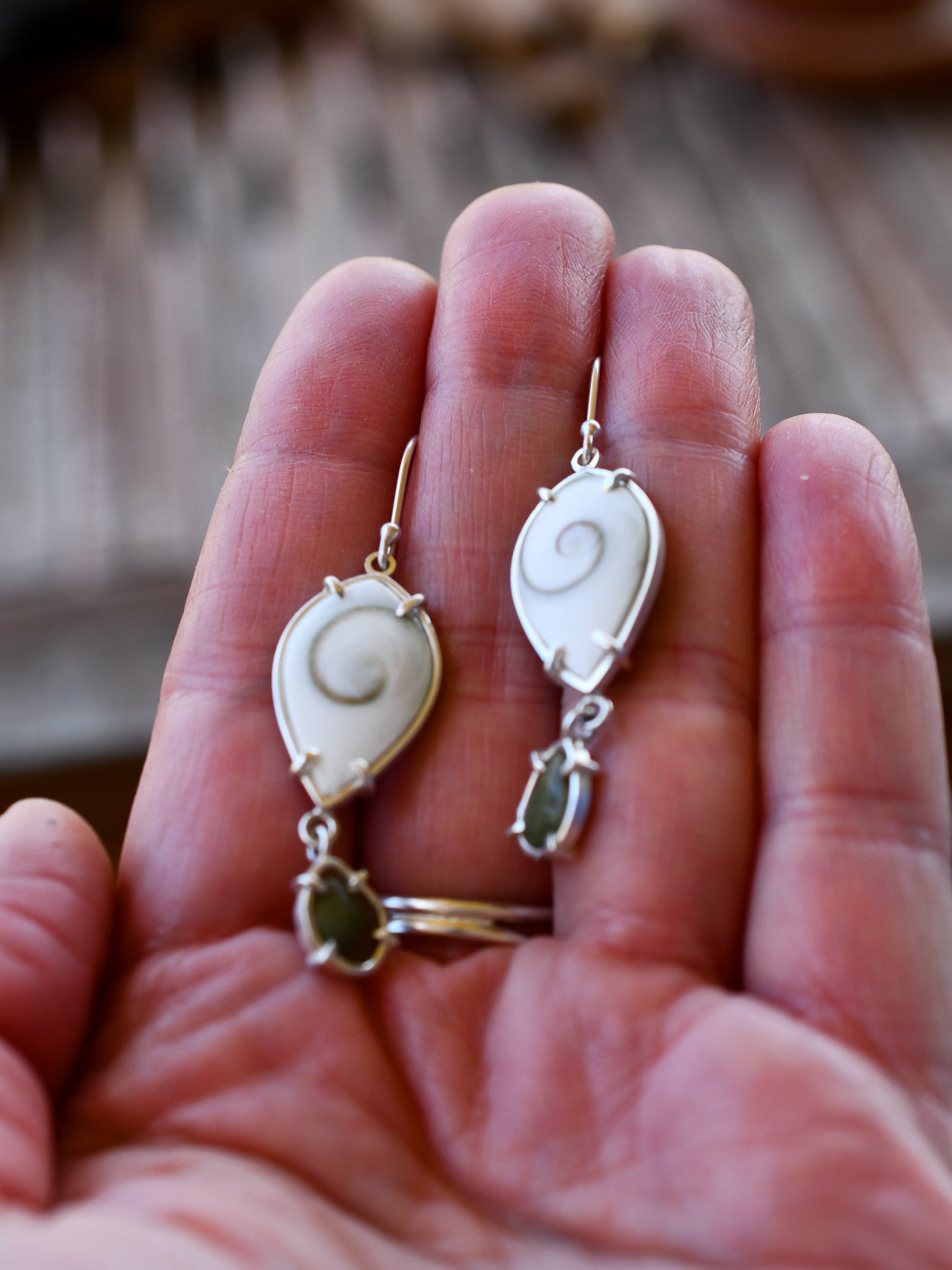 Hand holding a pair of shell and beach stone earrings with a blurred natural background