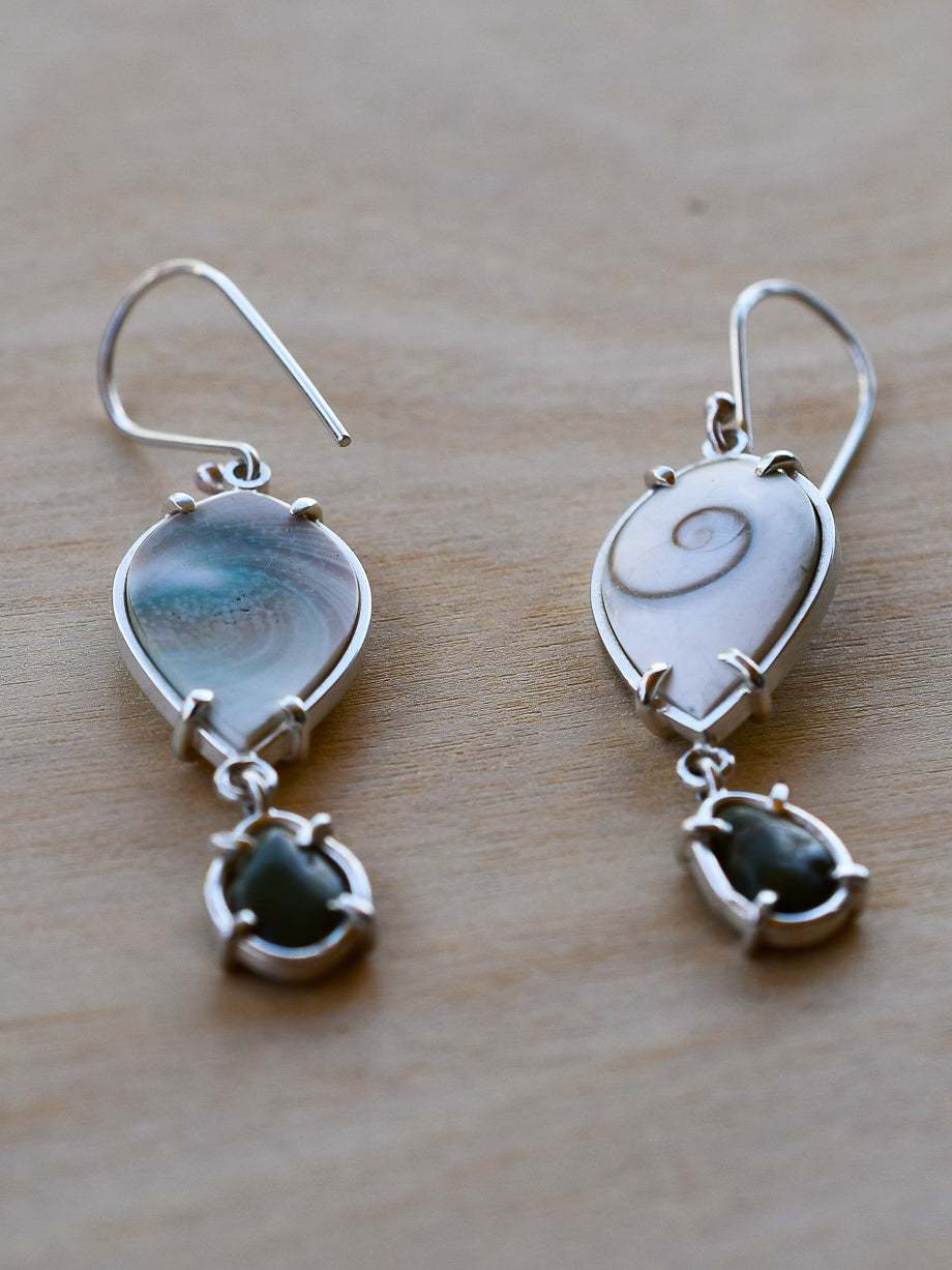 Pair of silver earrings with shells and beach stones on a wooden surface