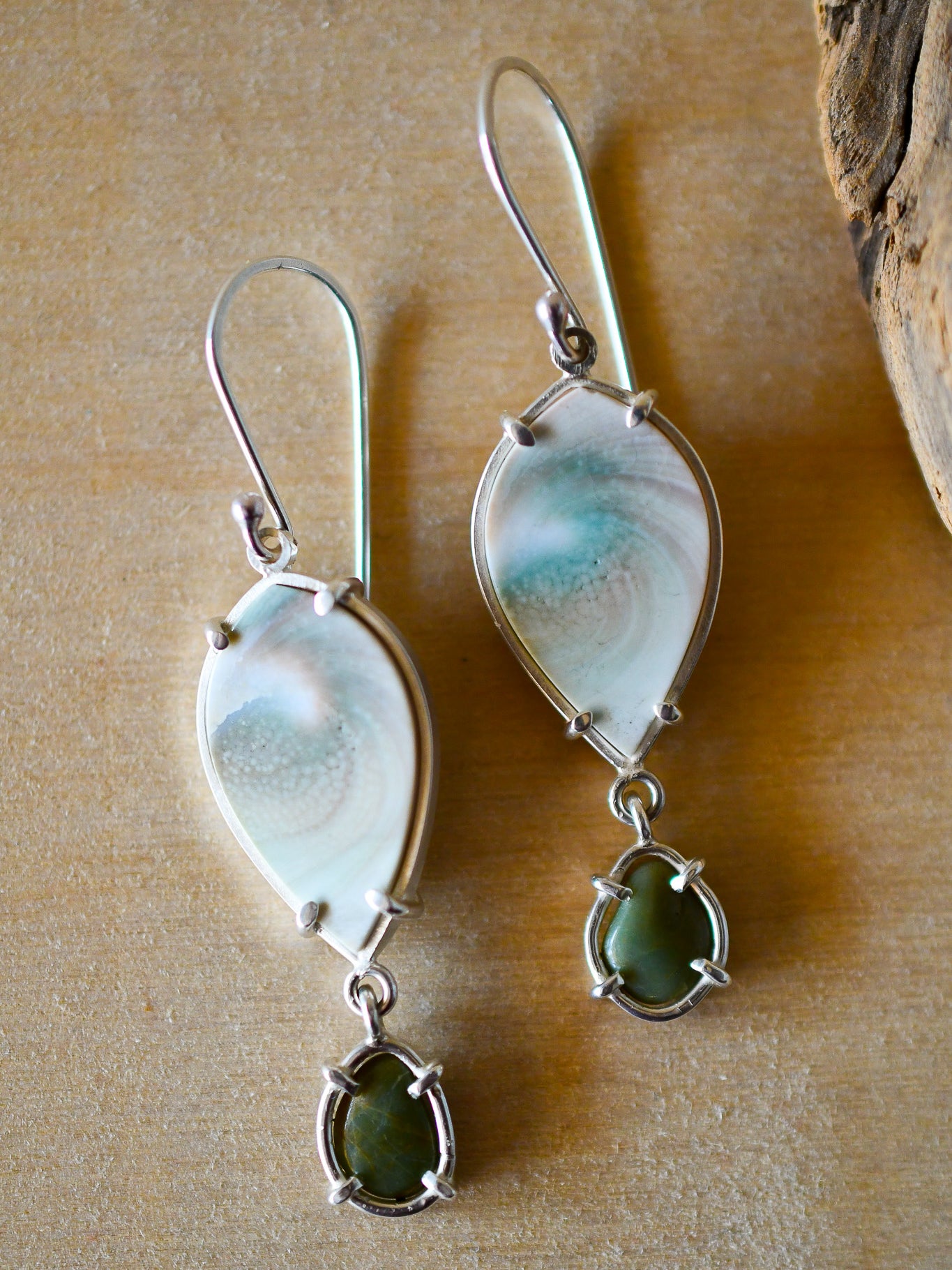 Pair of earrings with white shell and green beach stones on a wooden surface
