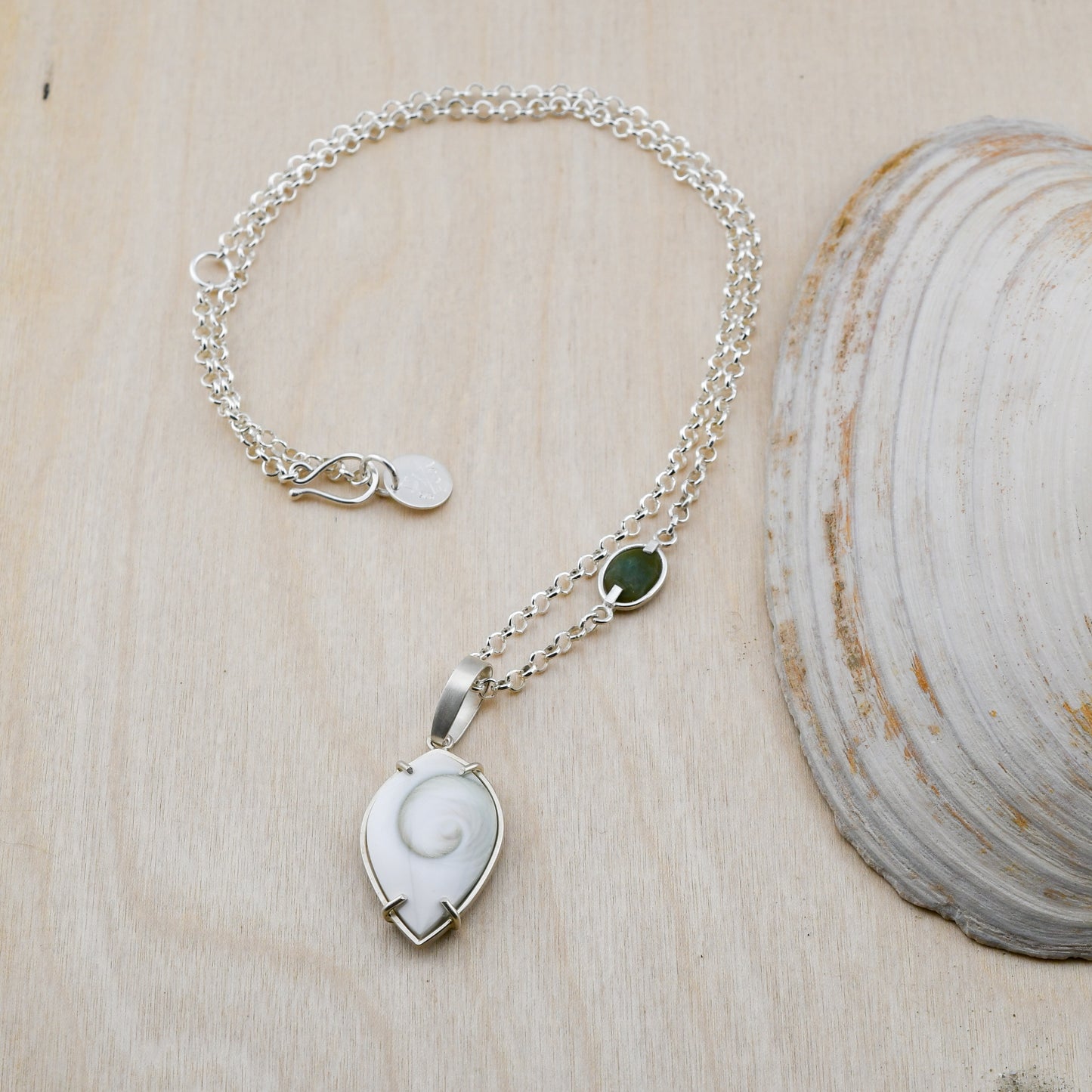 Silver necklace with green beach stone and Spiral Shiva shell pendant on a neutral background