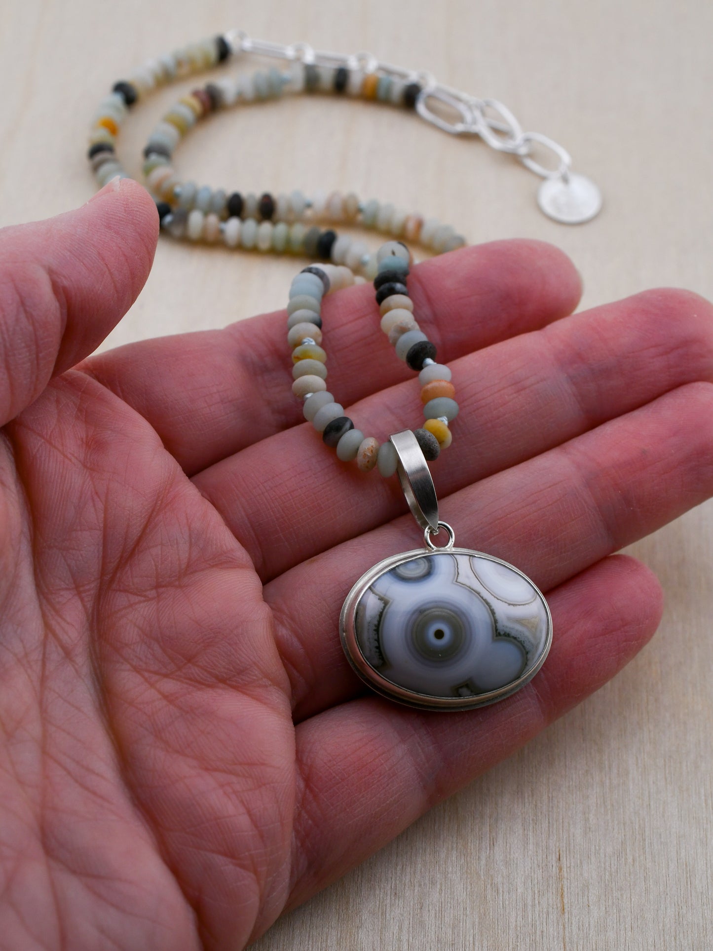 Amazonite beaded necklace with an ocean jasper pendant held in a hand on a light wooden surface