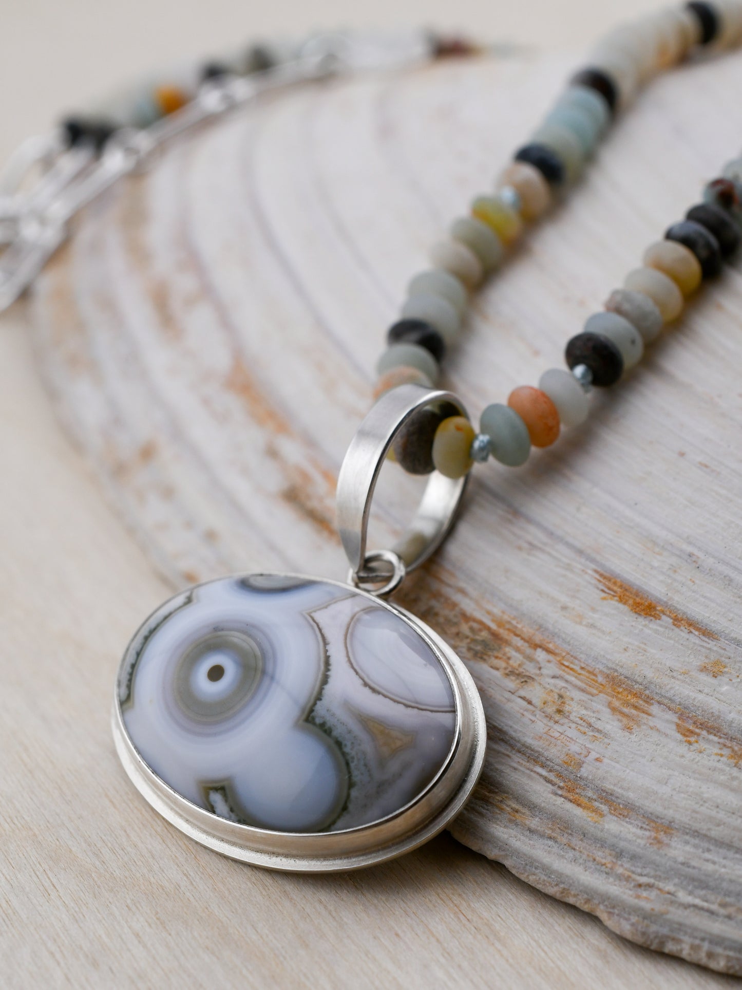Amazonite beaded necklace with an ocean jasper pendant on a shell and wooden surface