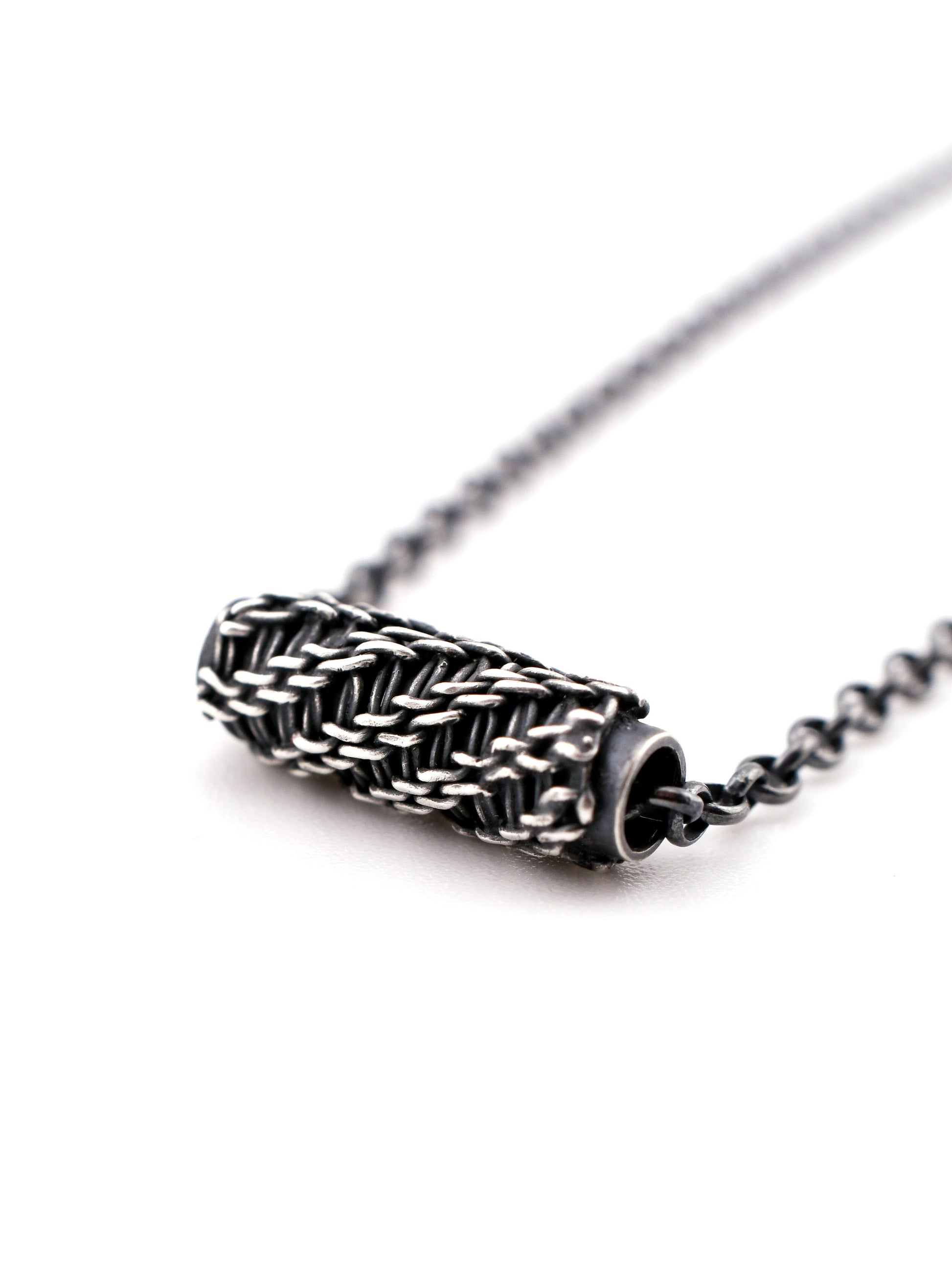 Close-up of a silver necklace with a woven design on a white background