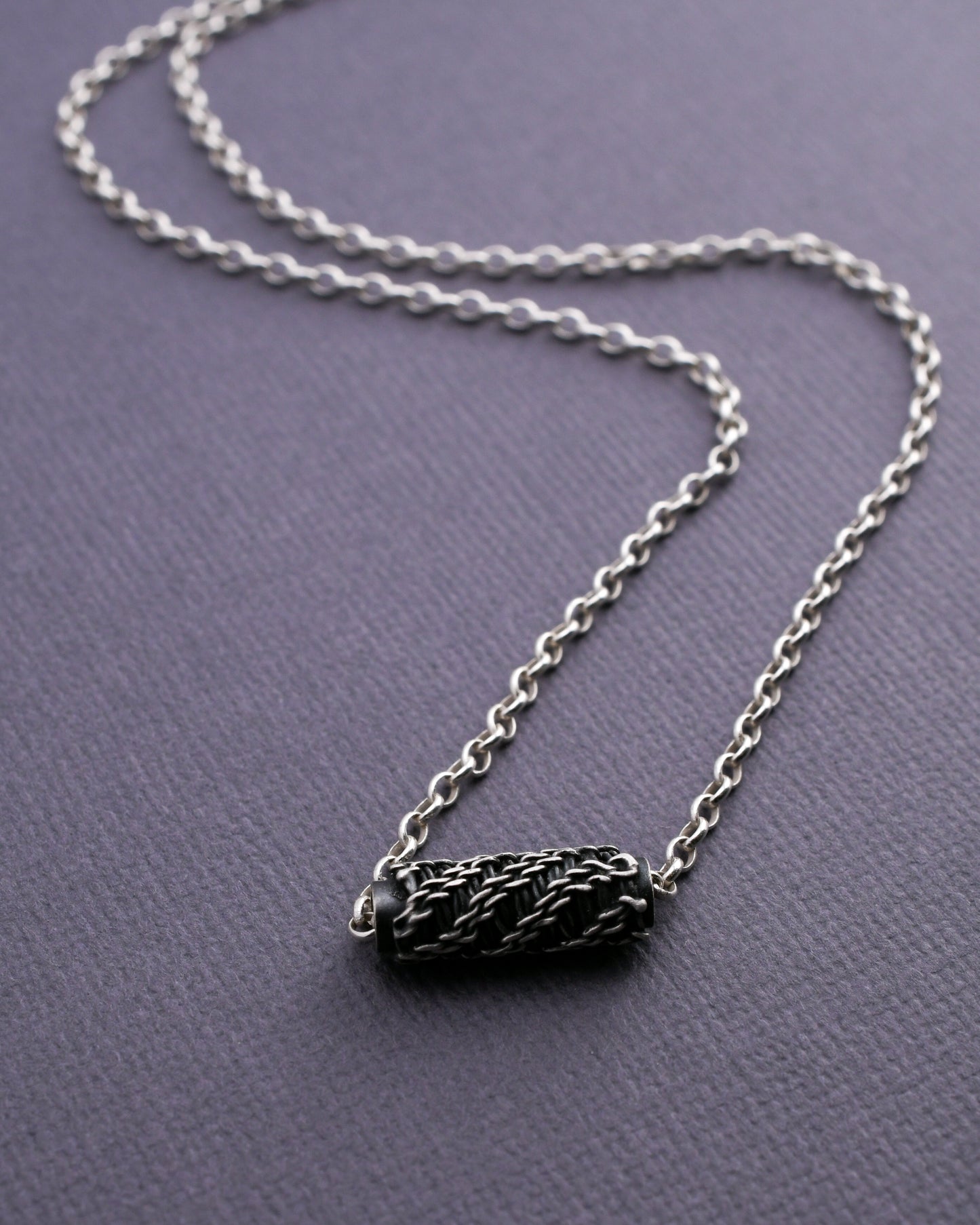 Black woven bead necklace on a bright silver chain displayed on a  textured surface