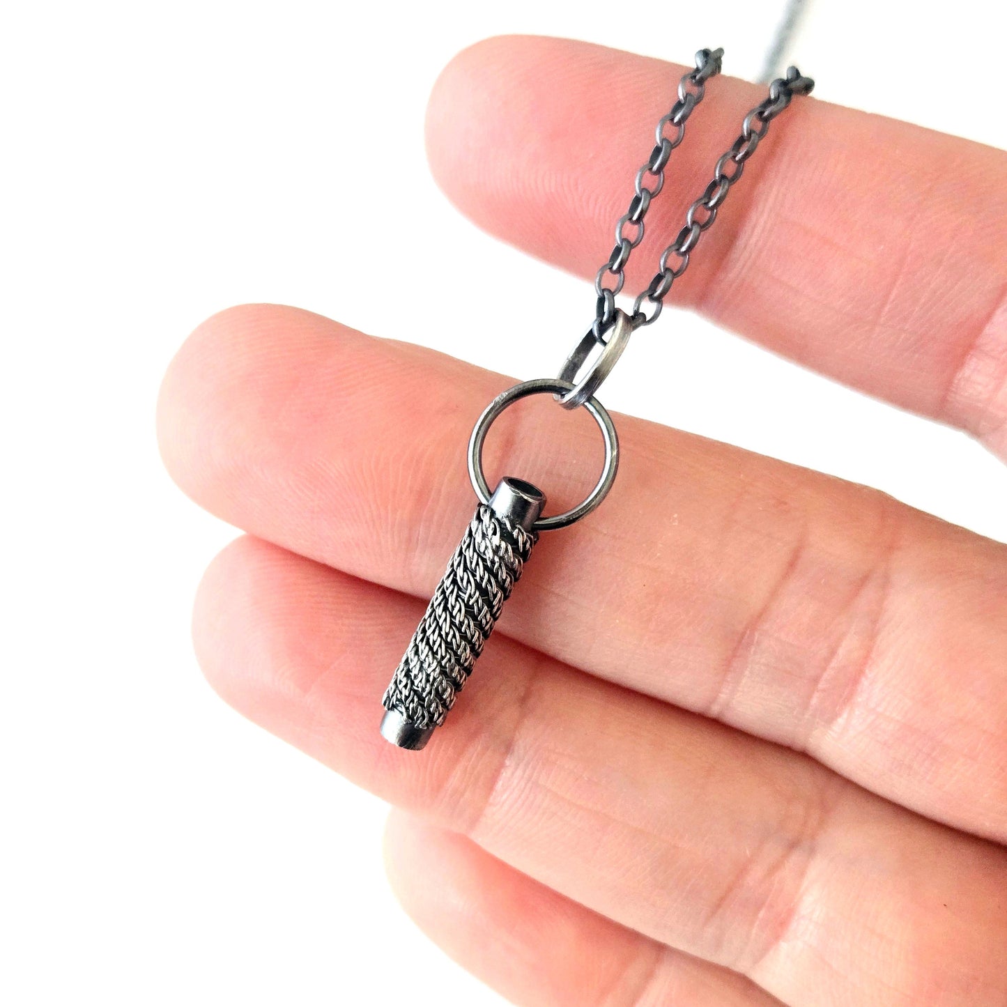 Silver pendant necklace held between fingers on a white background