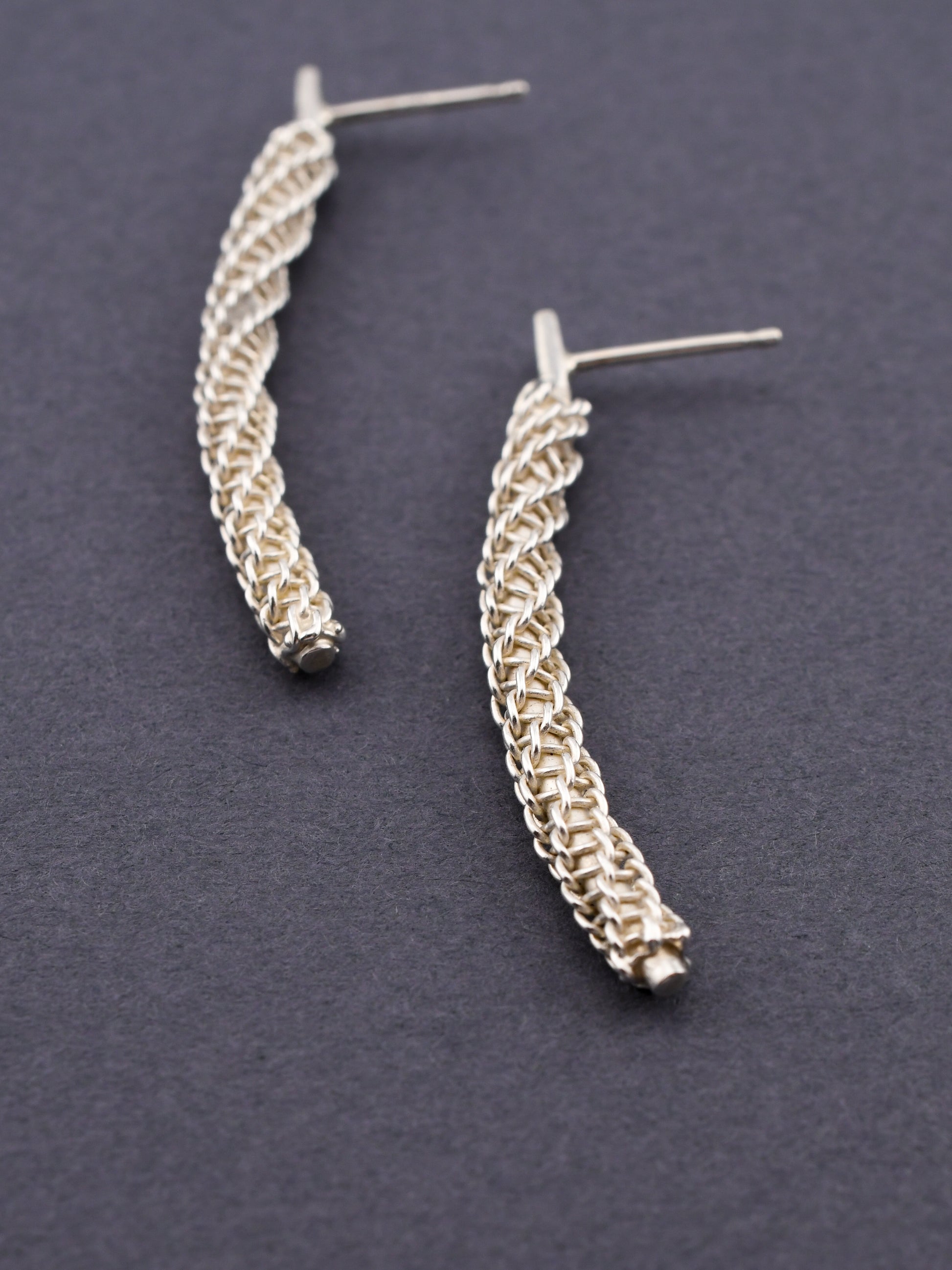 Pair of silver woven earrings on a dark gray background