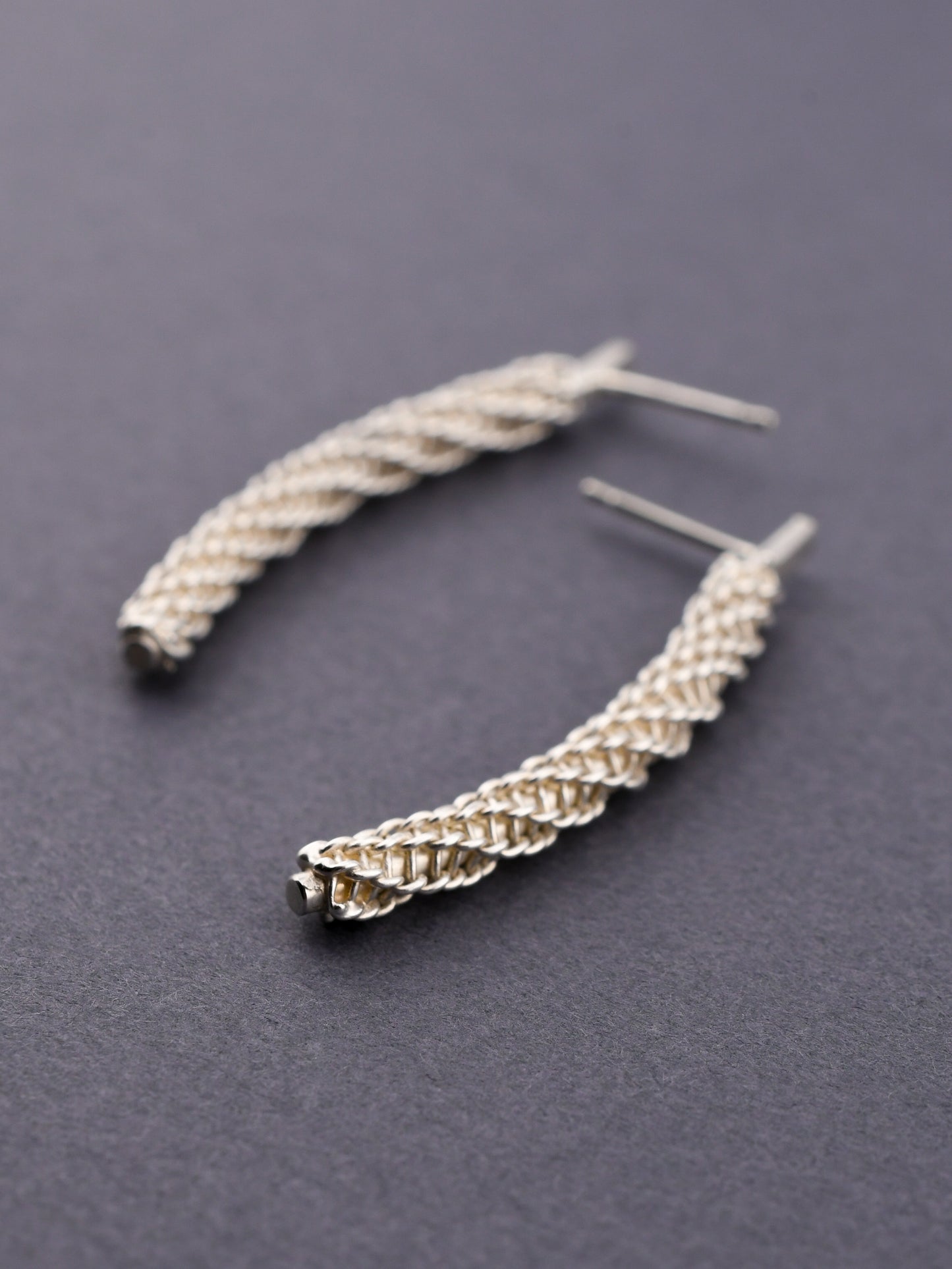 Silver braided earrings on a dark gray background