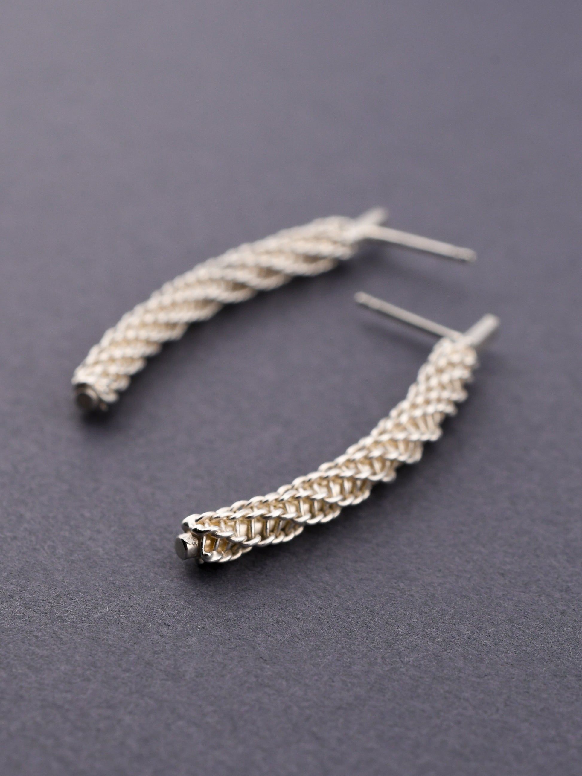 Silver braided earrings on a dark gray background