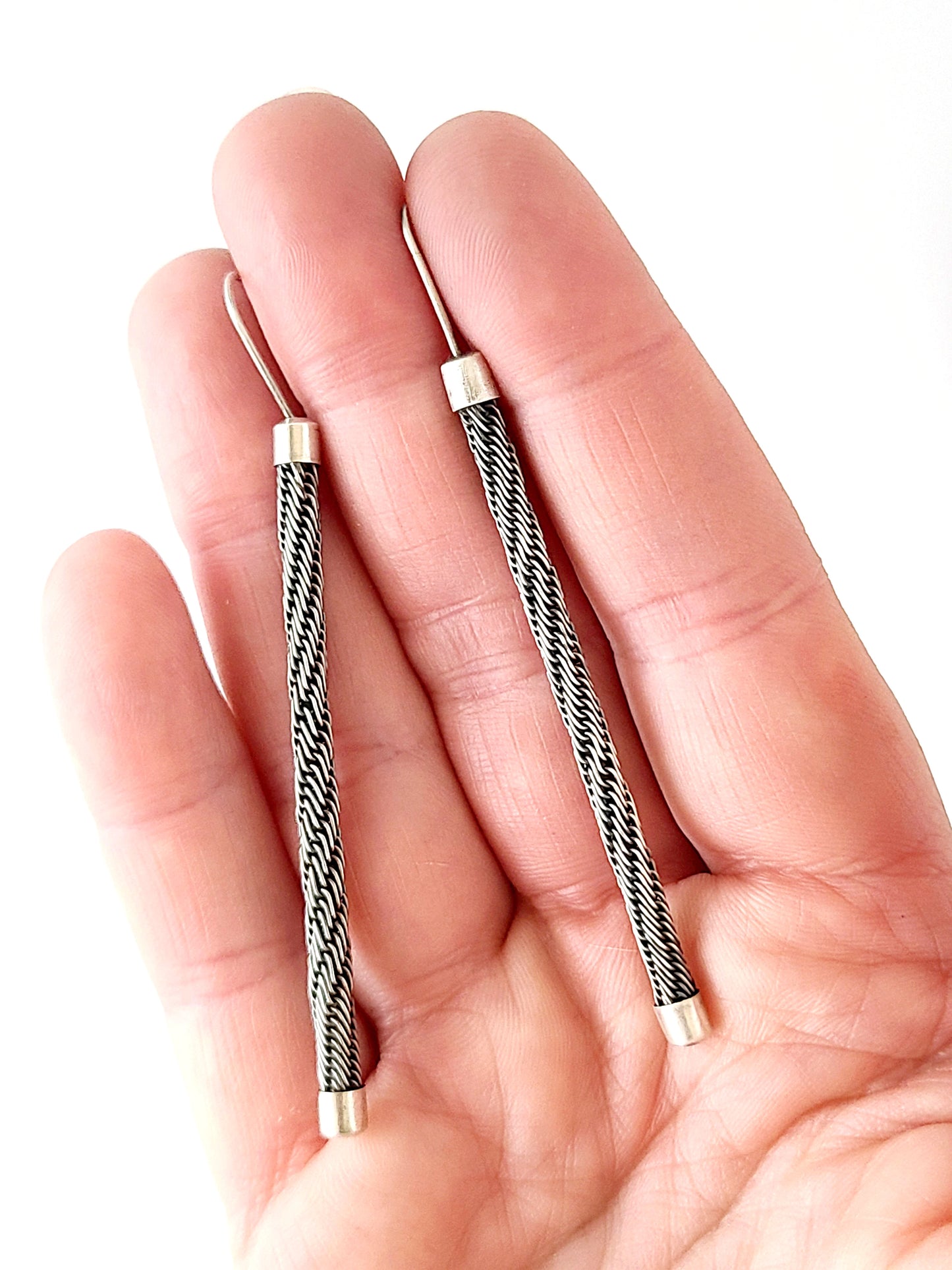 A pair of woven wire earrings held in a hand on a white background