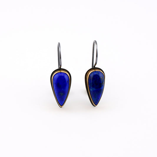 A pair of talon-shaped drop earrings featuring deep blue lapis lazuli stones set in 14k gold bezels with blackened silver ear wires, shown on a plain white background.