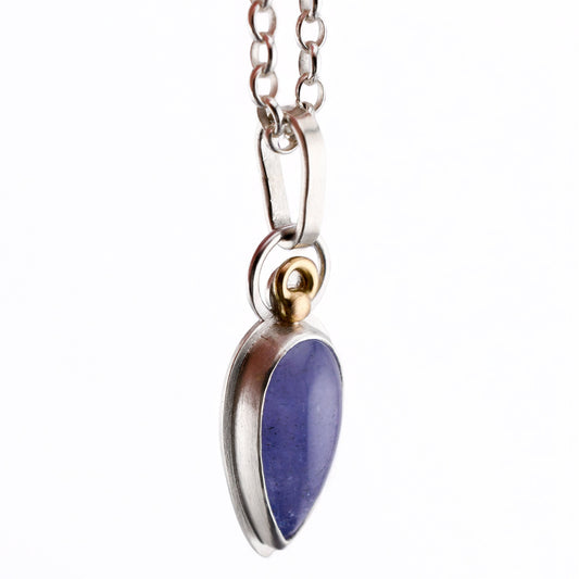 A blue-purple talon shaped Tanzanite pendant with 14k gold accents hangs from a silver chain over a white background