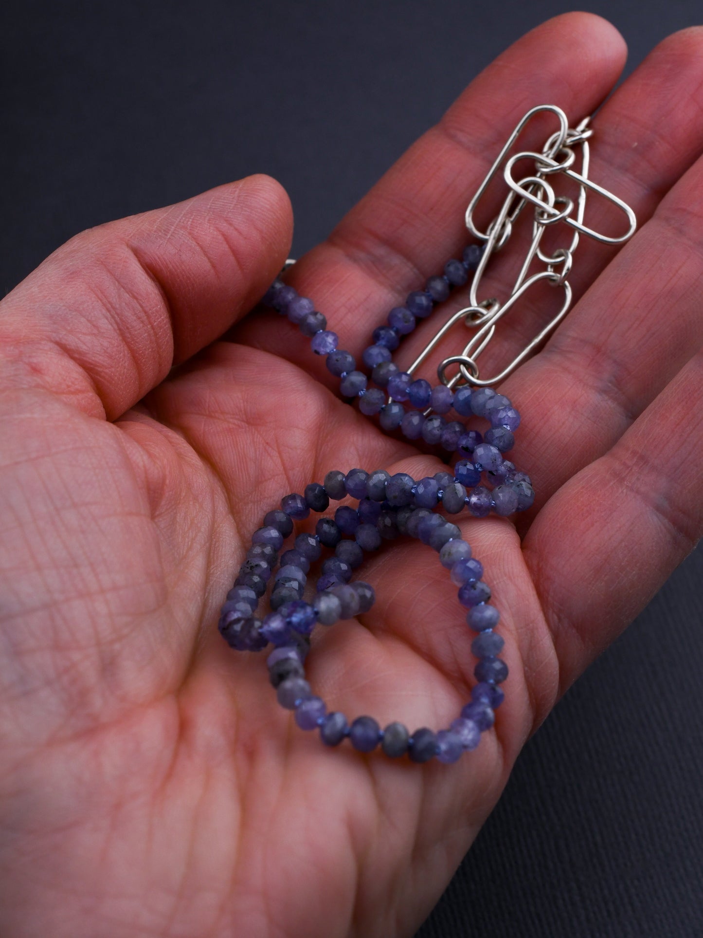 Hand holding a blue beaded necklace with a silver clasp against a dark background