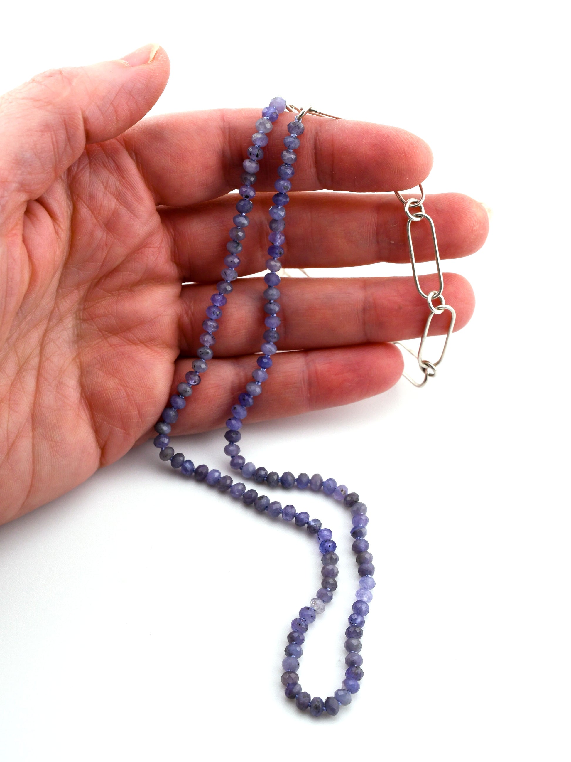 Hand holding a blue beaded necklace with a silver chain on a white background