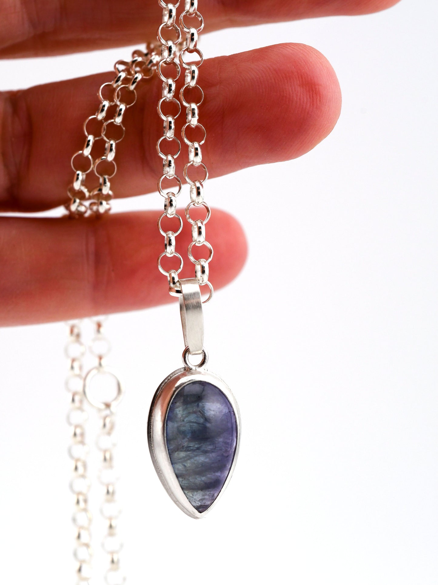 Teardrop-shaped blue- purple stone pendant on a silver chain held by a hand against a white background