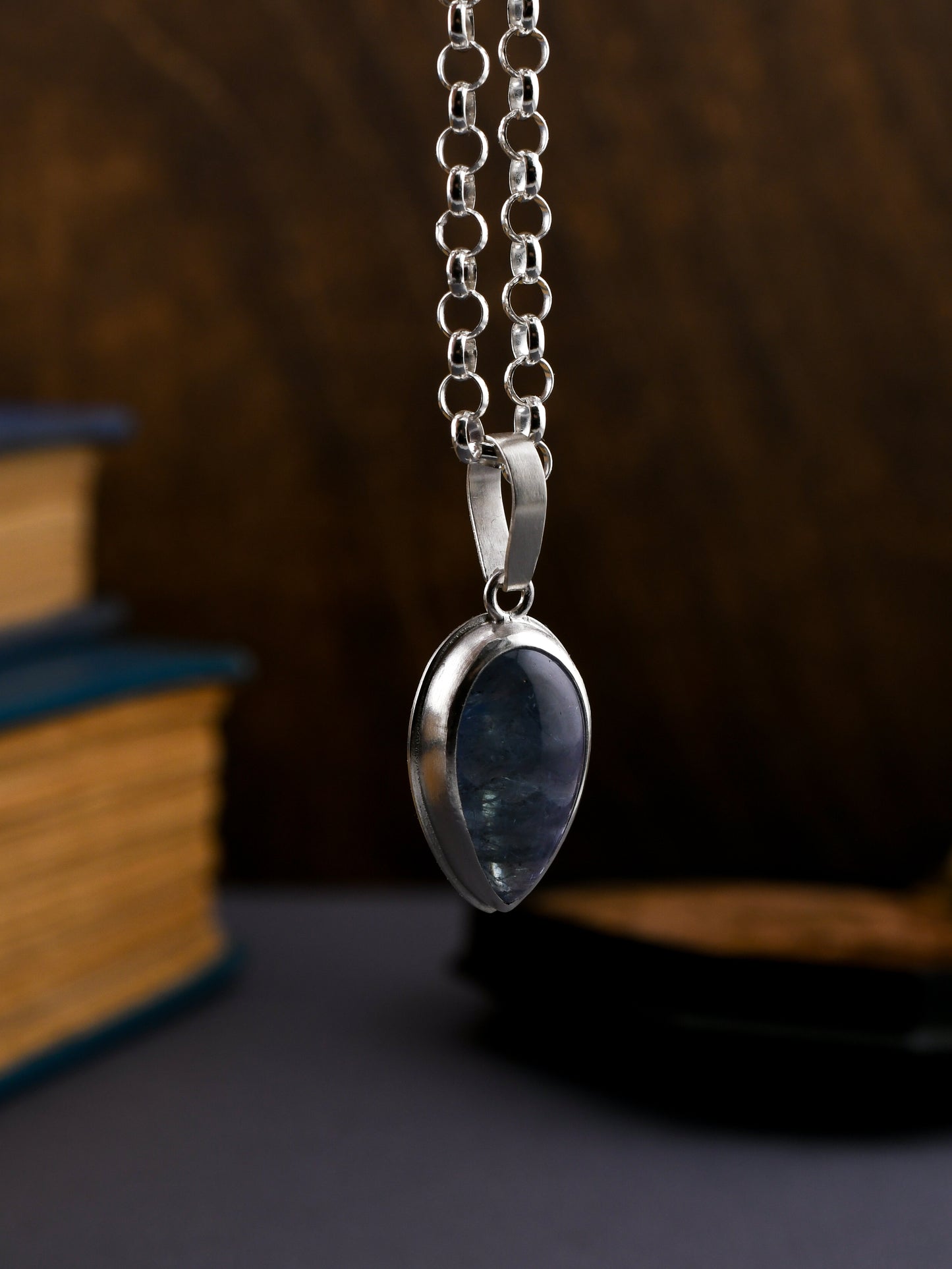 Necklace with a blue pendant on a chain against a dark background with books.