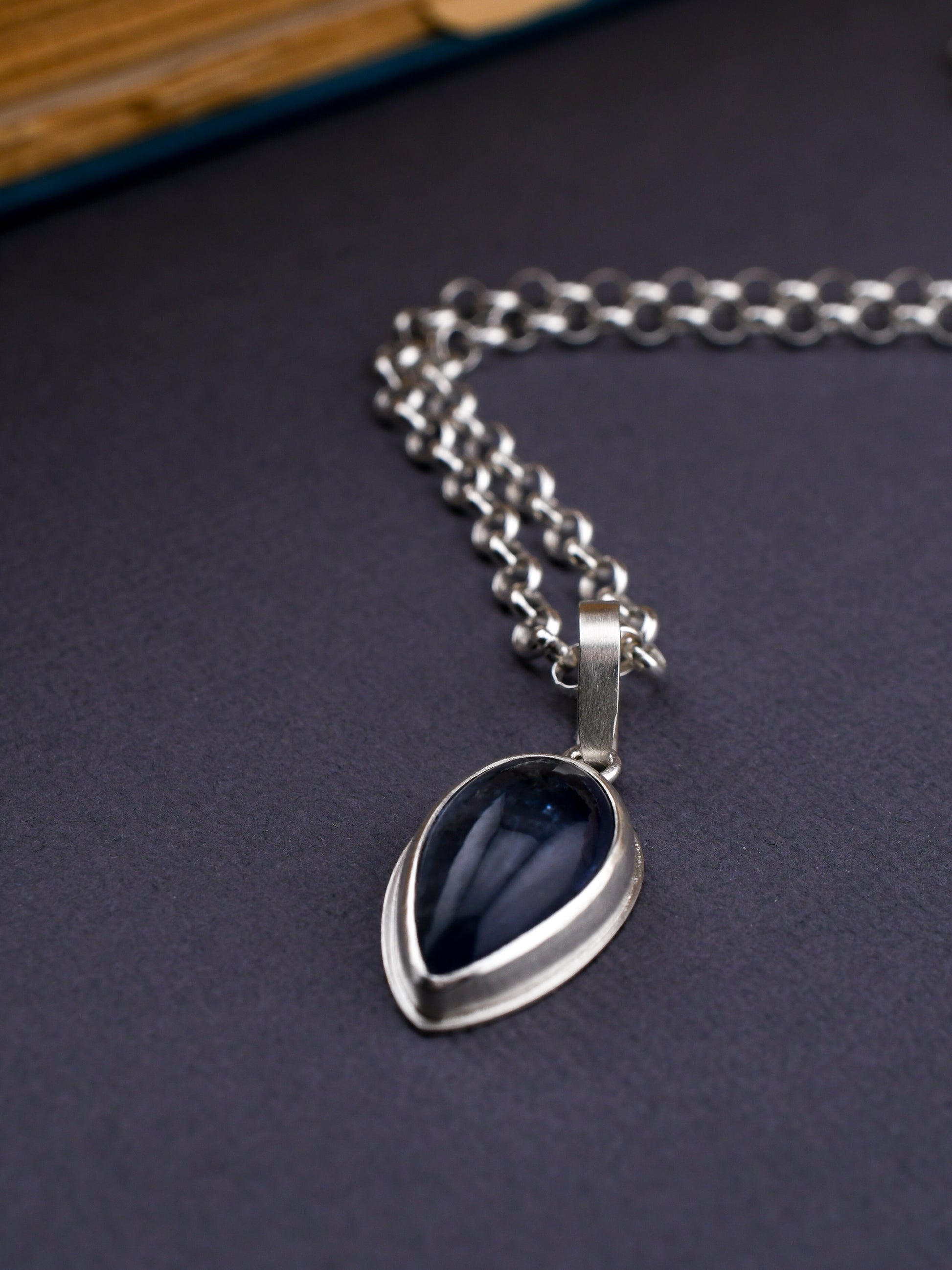 Silver necklace with a blue pendant on a dark surface