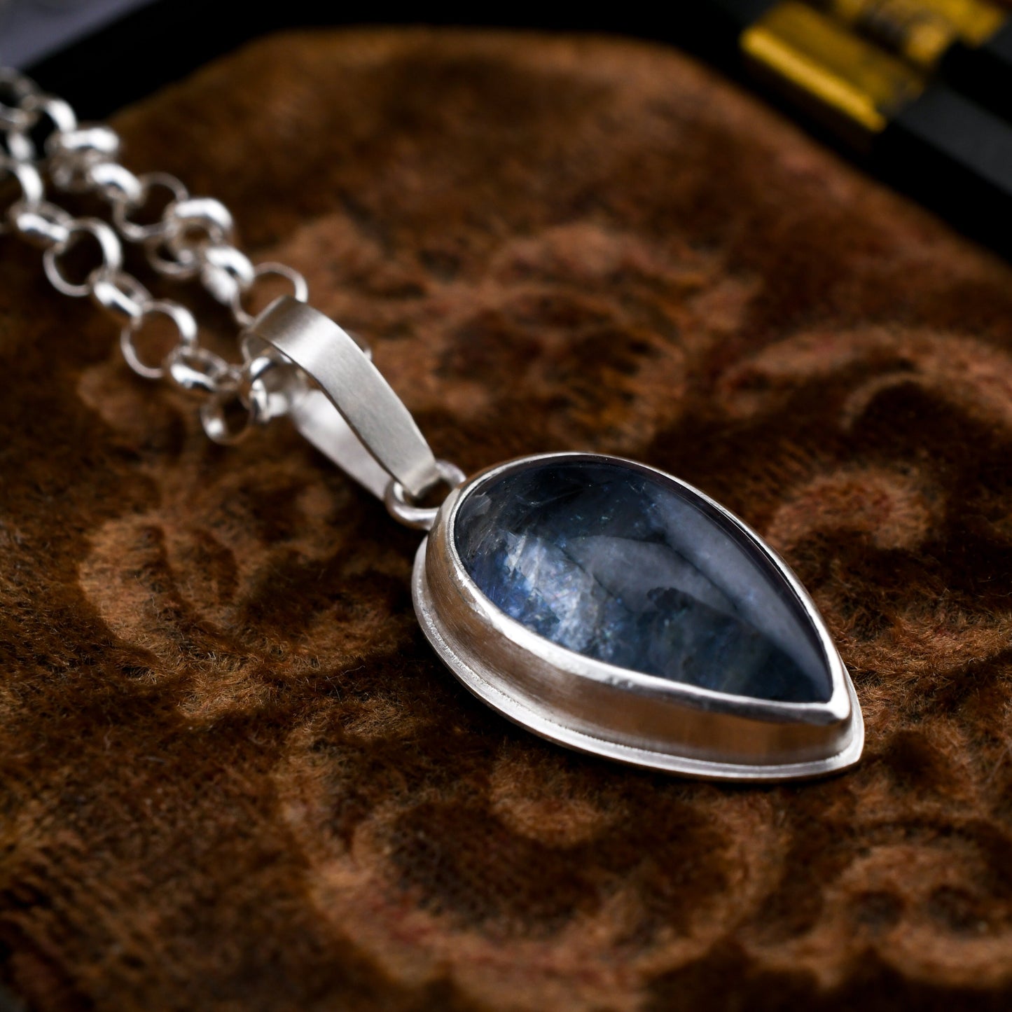 Silver necklace with a blue teardrop pendant on a textured brown surface