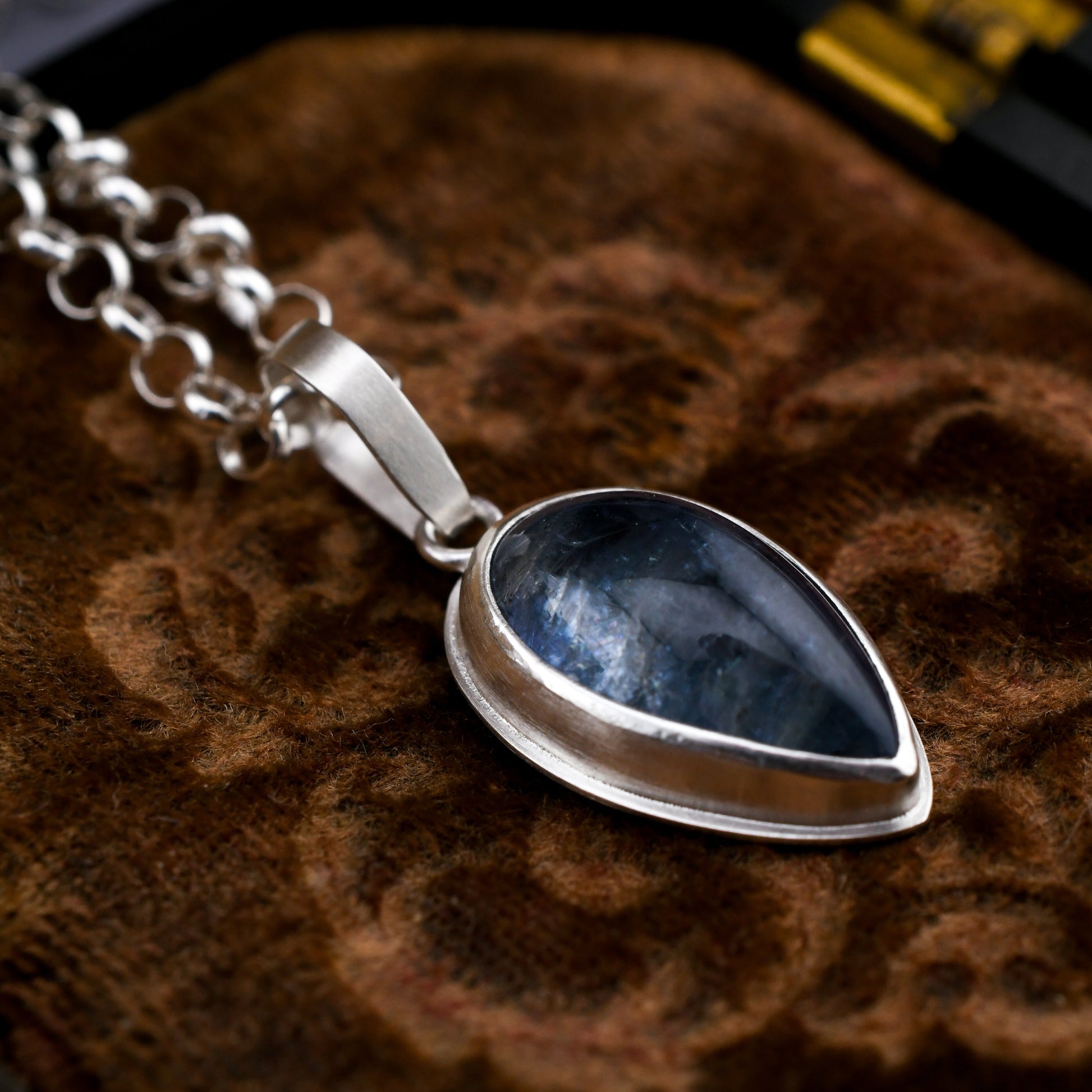 Silver necklace with a blue teardrop pendant on a textured brown surface
