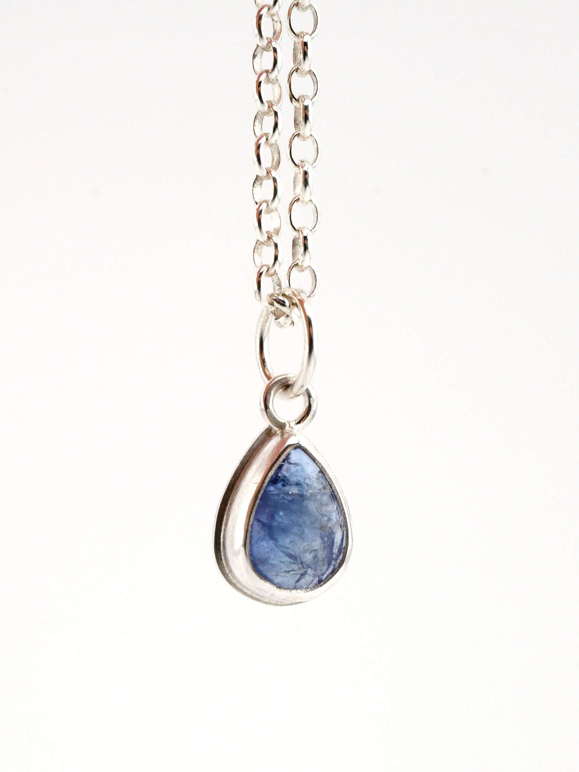 Teardrop-shaped blue stone pendant on a silver chain against a white background