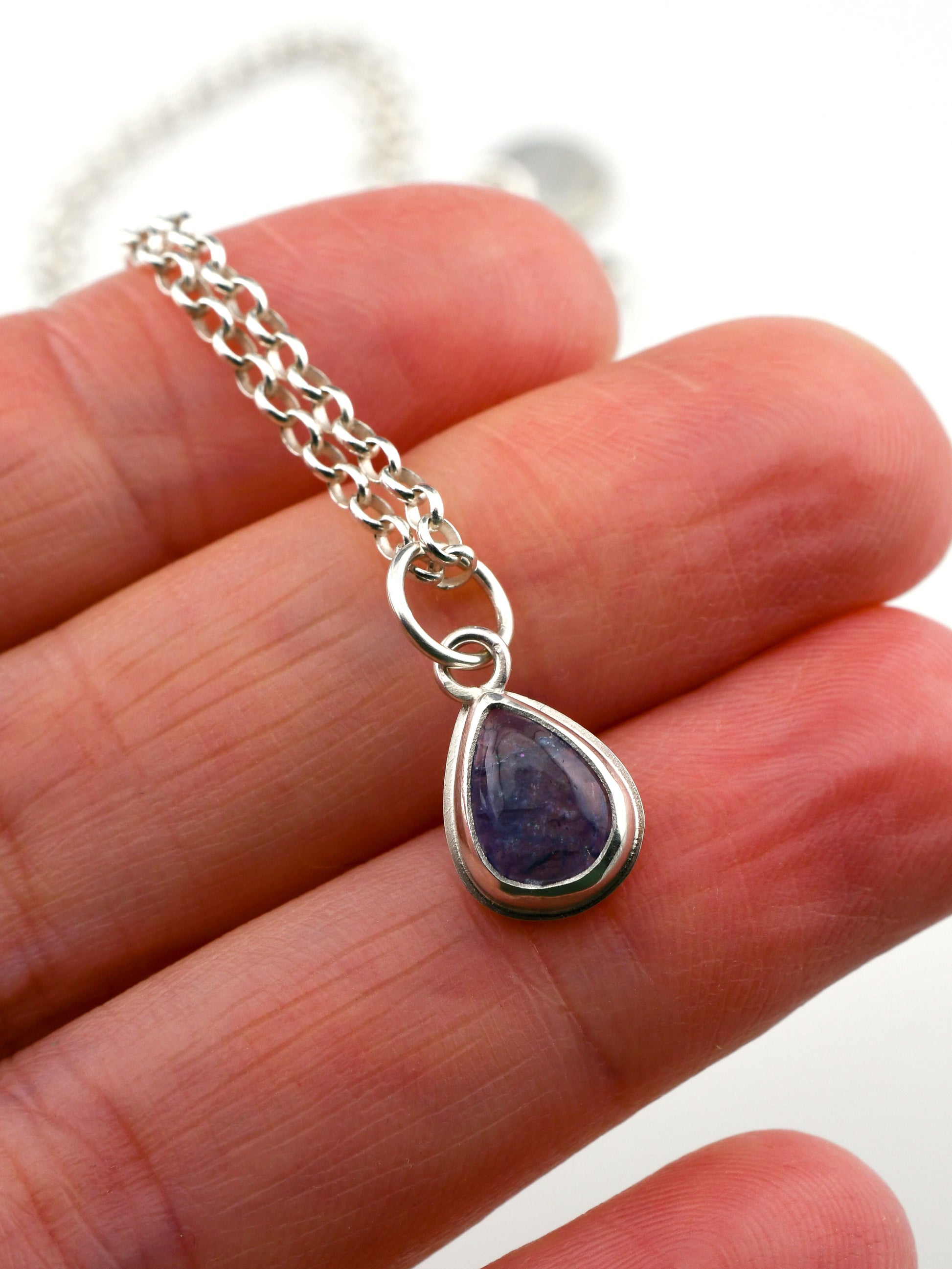 Teardrop-shaped blue-purple gemstone pendant on a silver chain held in hand