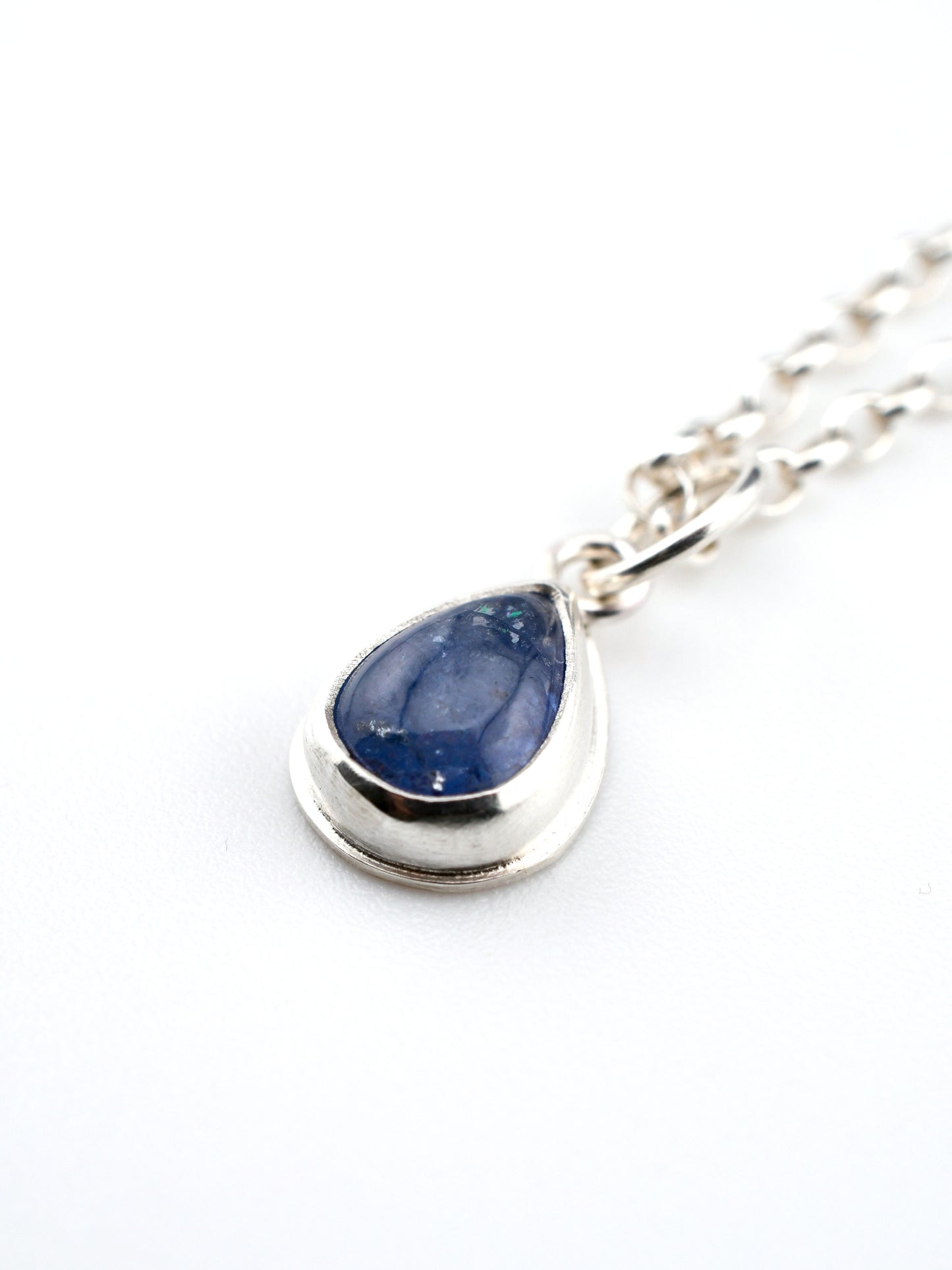 Teardrop-shaped blue stone pendant on a silver chain against a white background