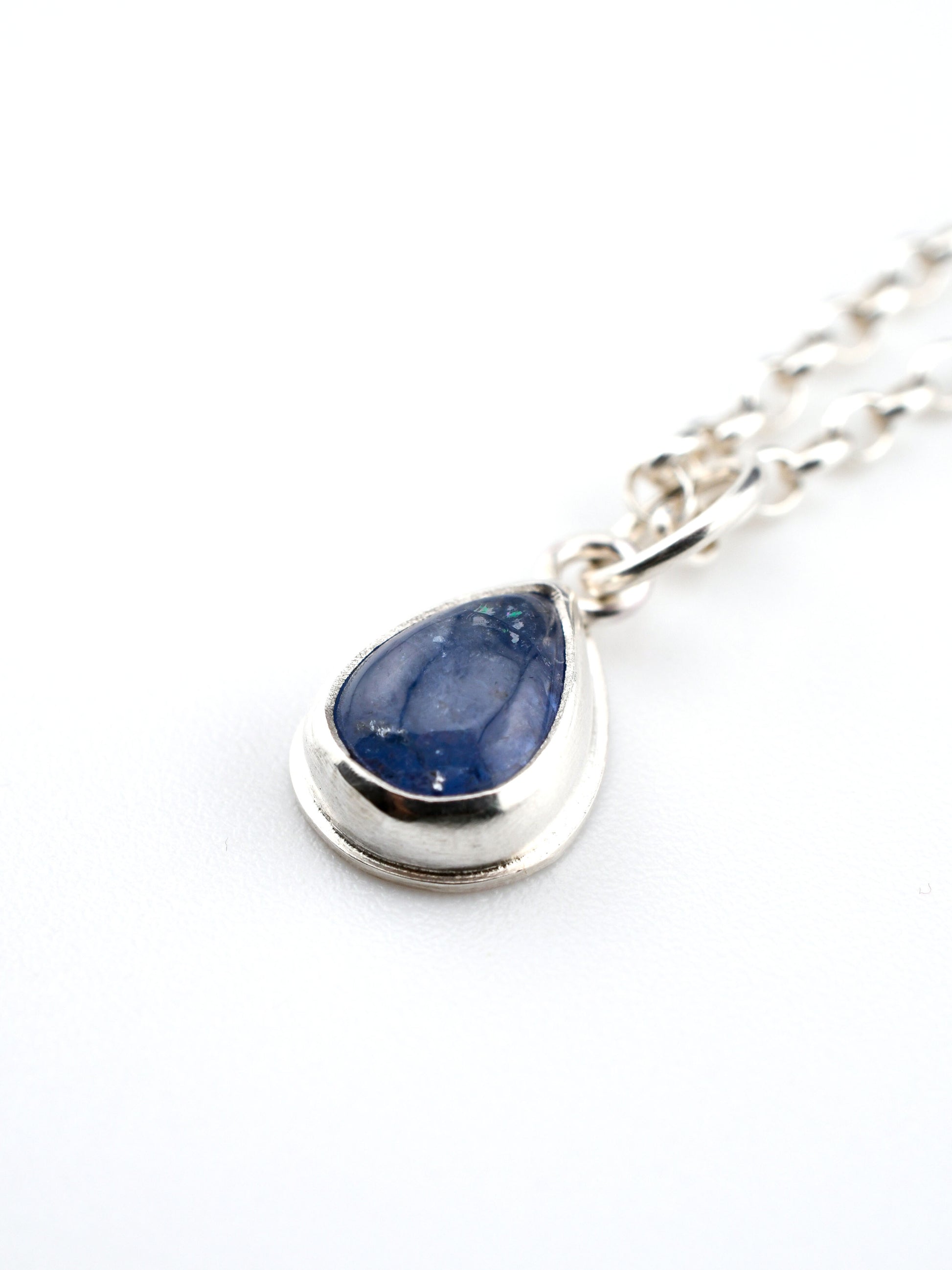 Teardrop-shaped blue stone pendant on a silver chain against a white background