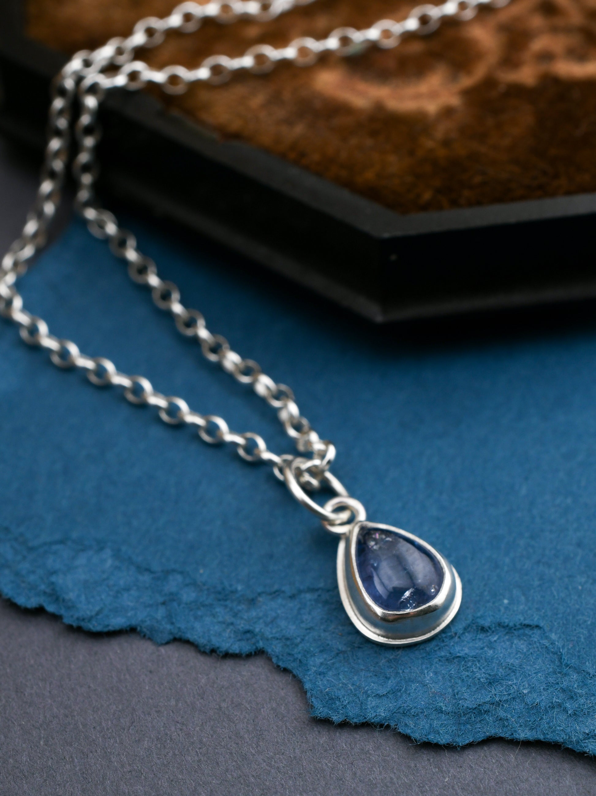 Silver necklace with a teardrop-shaped pendant on a blue fabric background