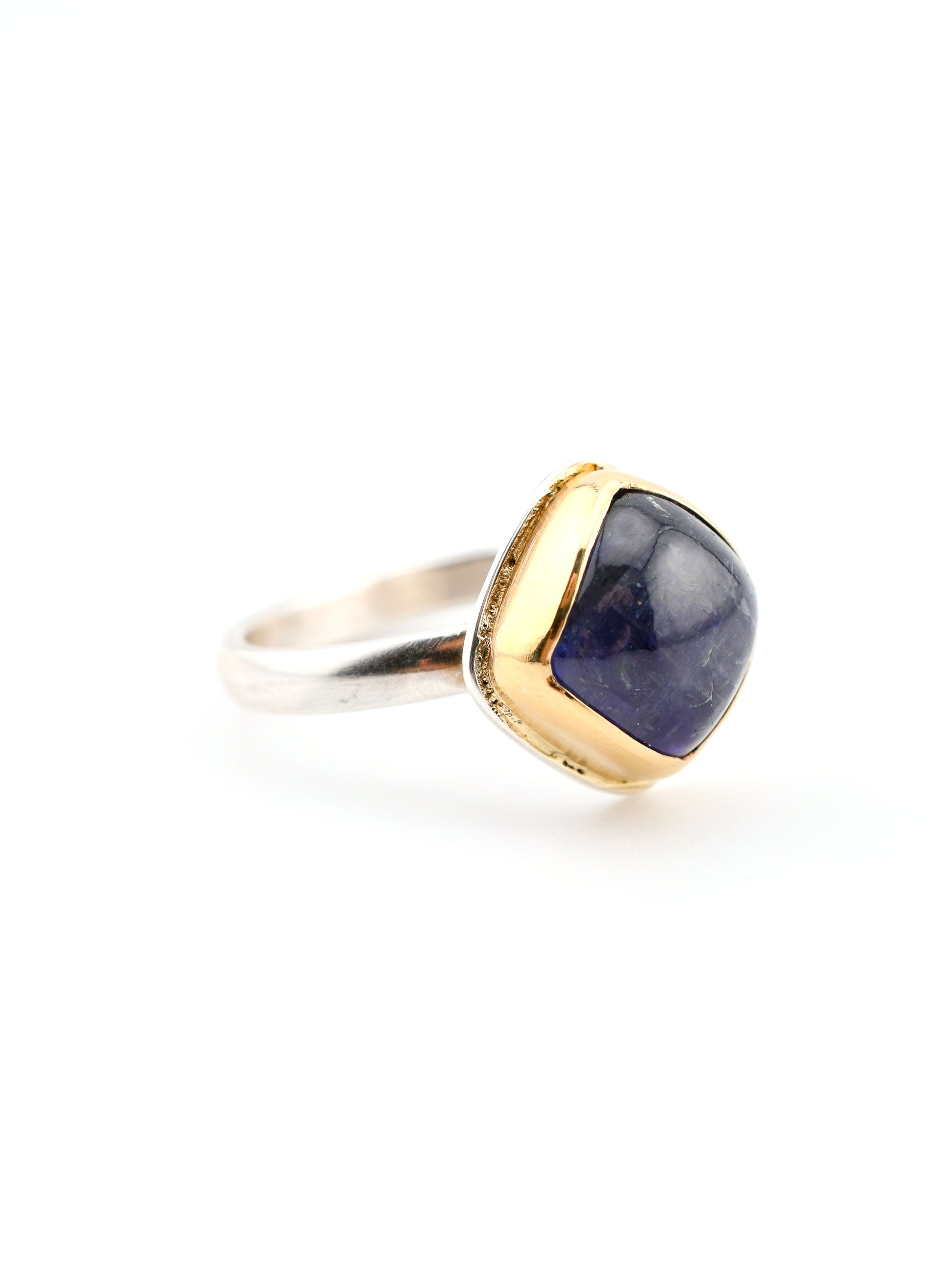 Ring with silver band and purple-blue stone set in gold on a white background