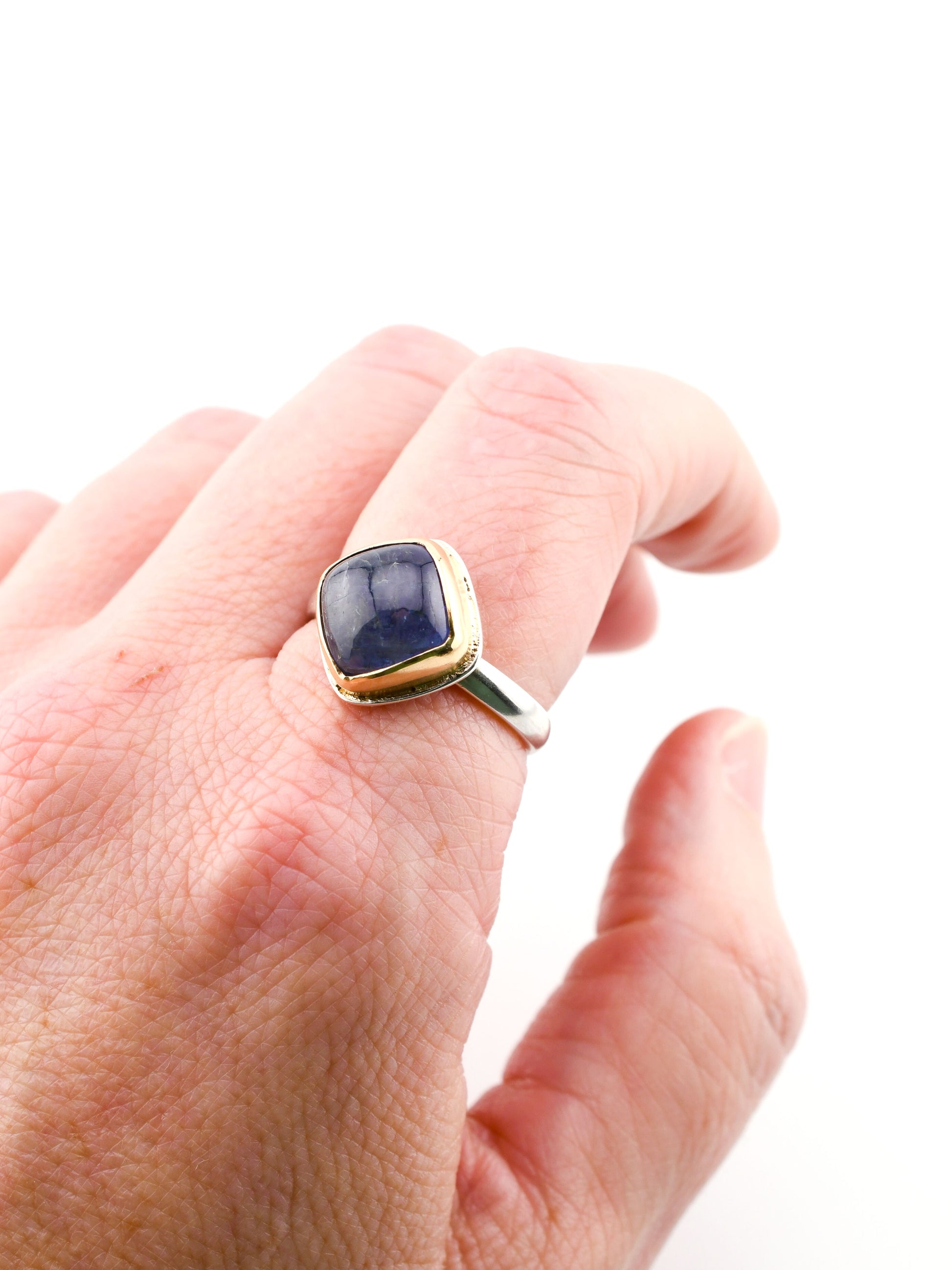 Gold ring with a blue stone on a person's finger against a white background
