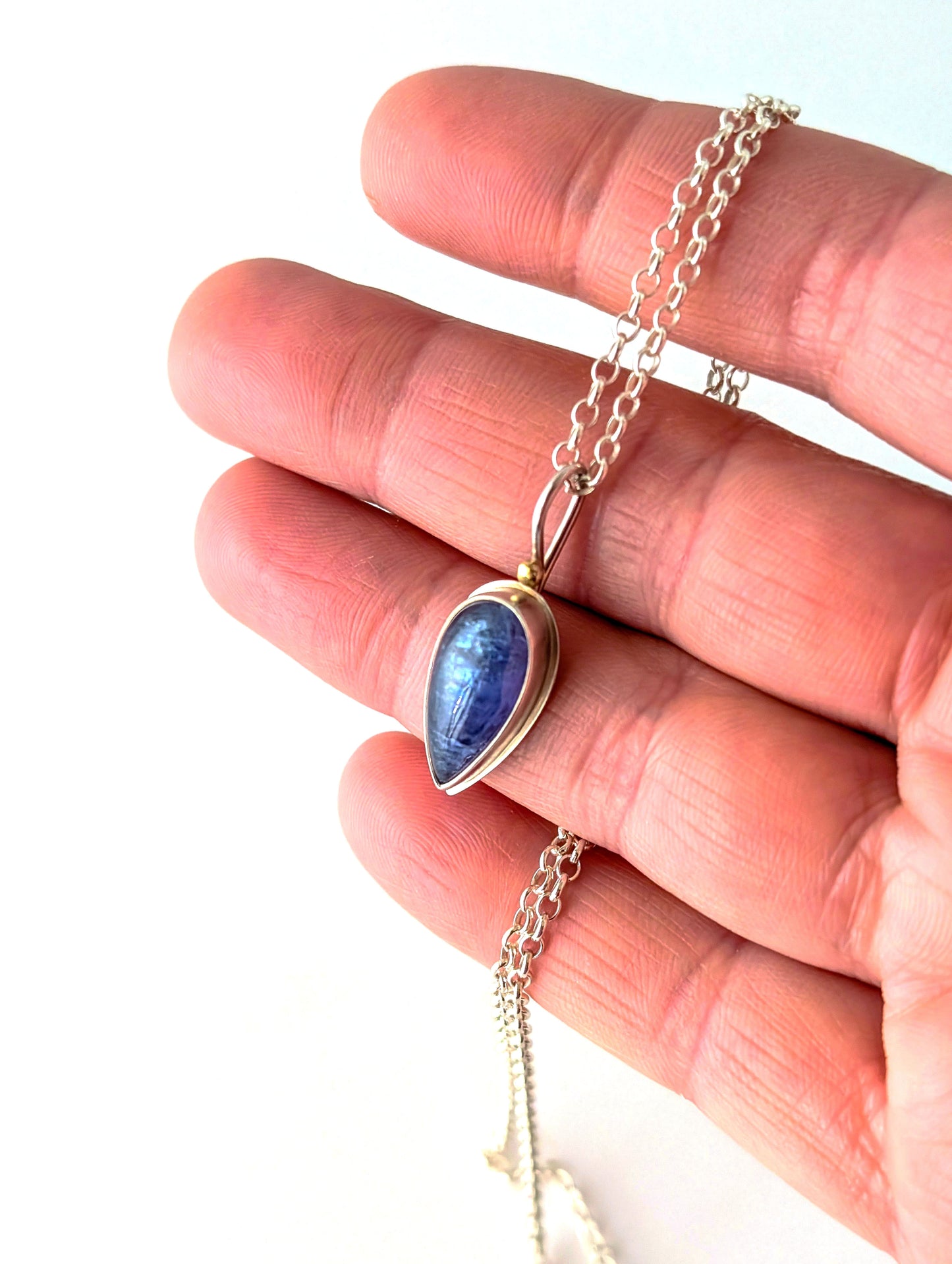 Hand holding a silver necklace with a blue teardrop pendant against a white background