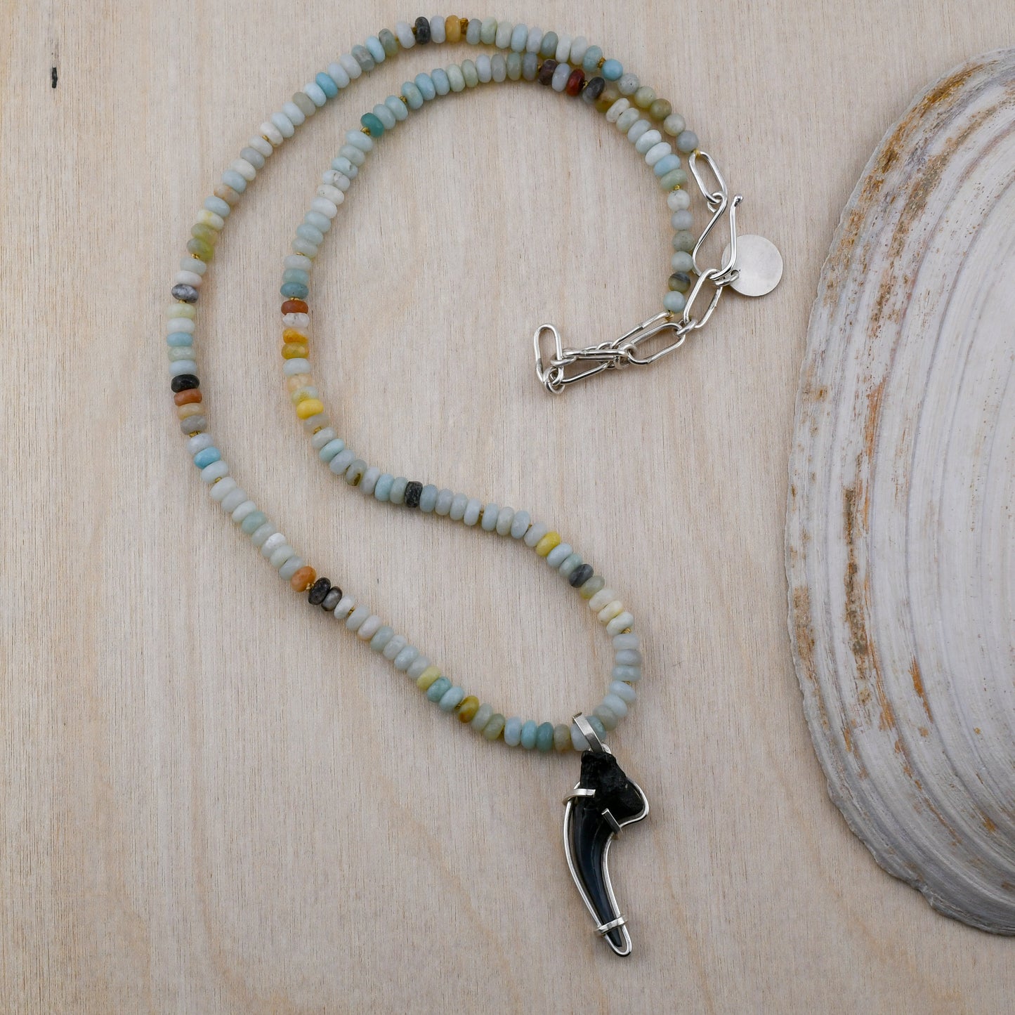 Necklace with beaded chain and shark tooth pendant on a wooden surface