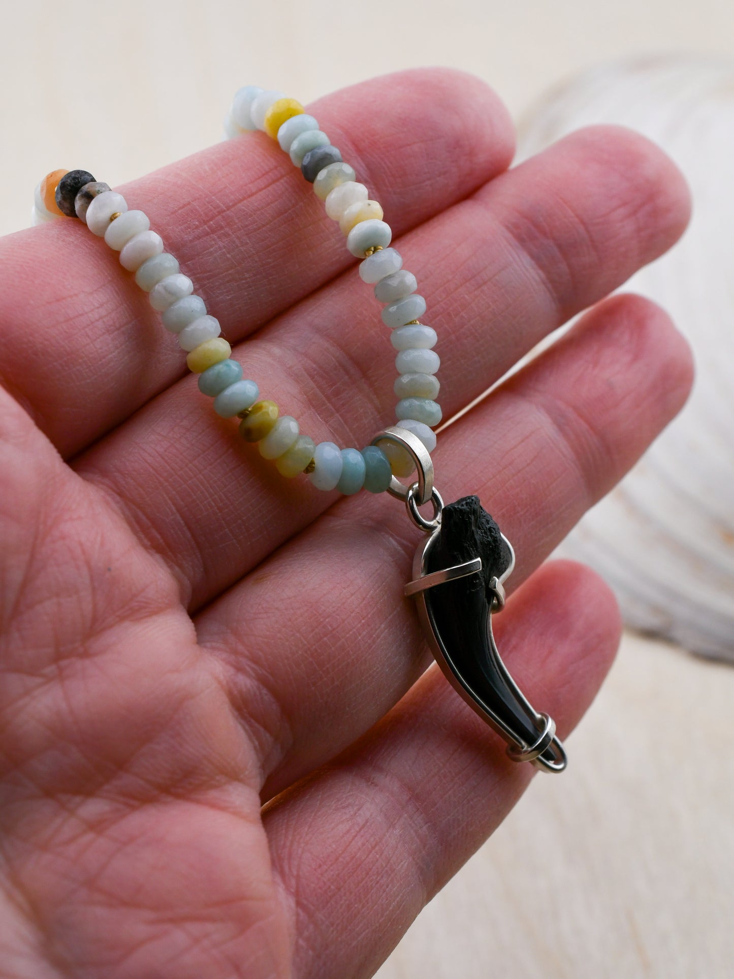 Beaded bracelet with a shark tooth pendant held in a hand against a neutral background