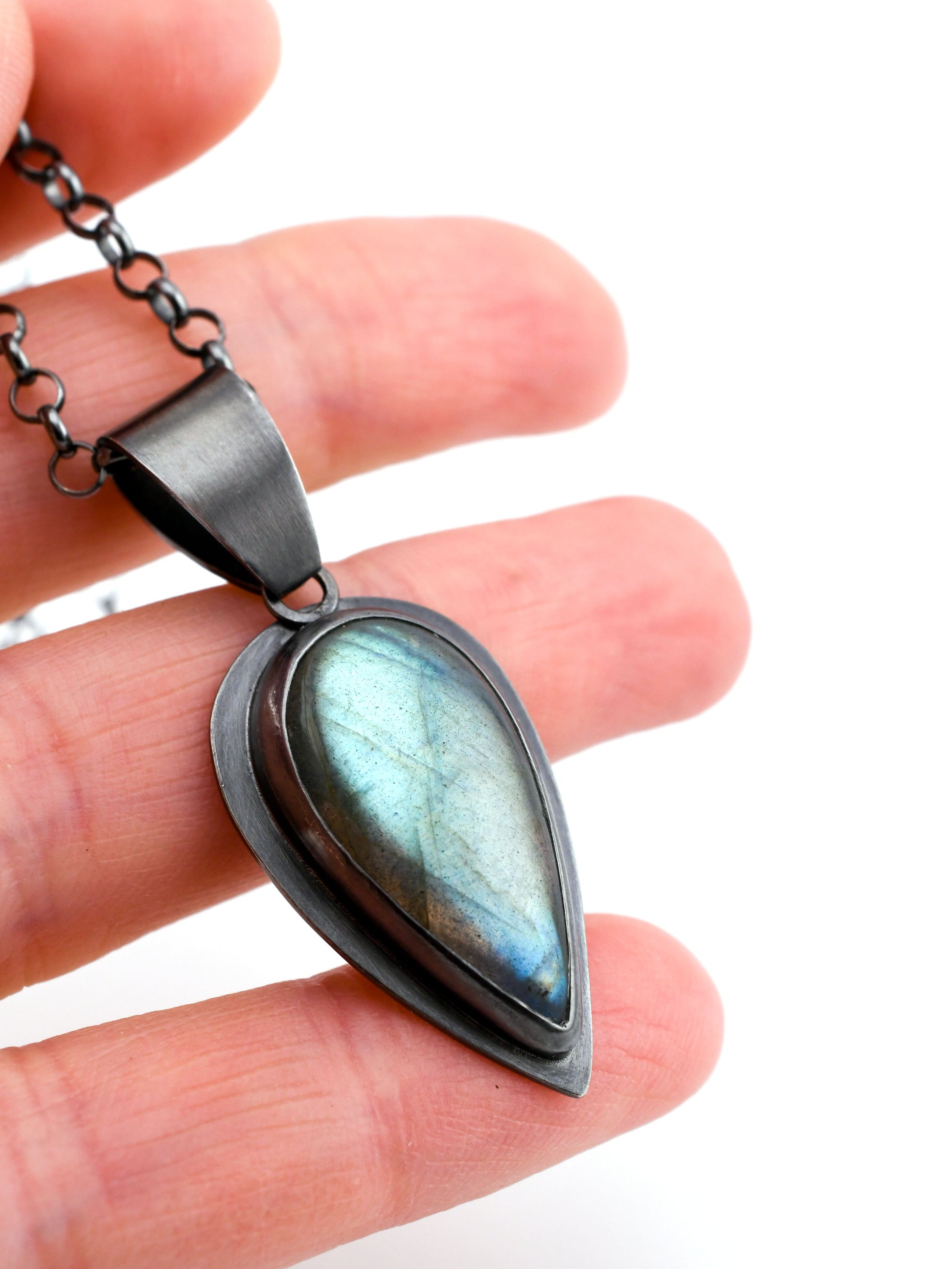 Teardrop-shaped pendant with a blue and green gemstone held between fingers on a white background