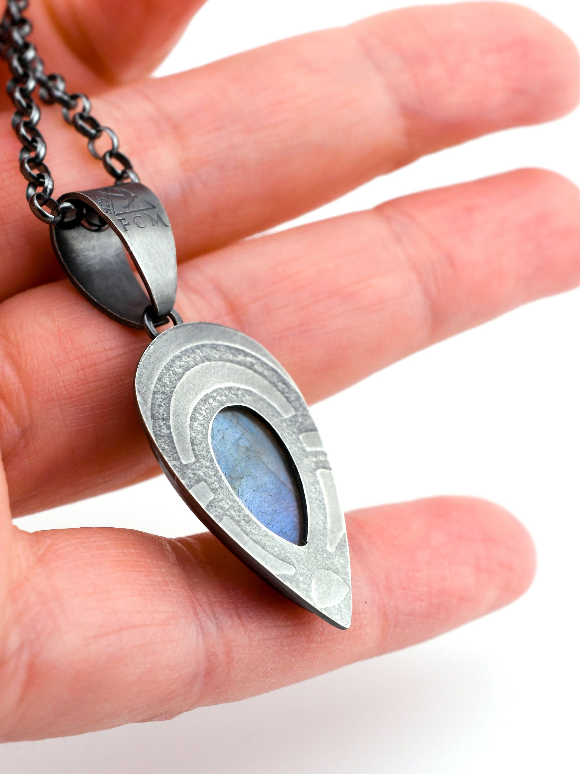 Hand showing the backside of a silver pendant with a blue stone against a white background