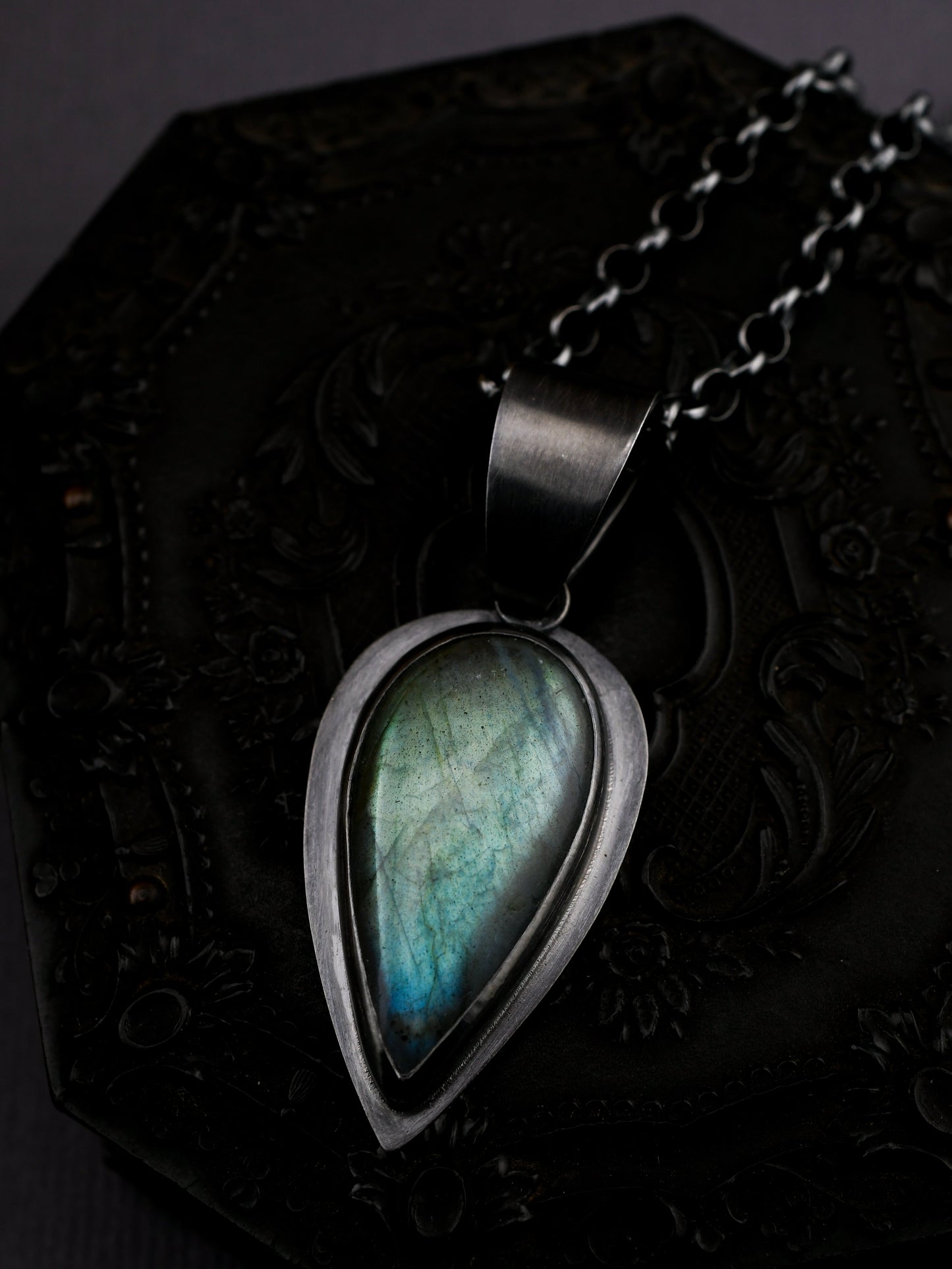 Teardrop-shaped pendant with a blue-green stone on a dark textured surface