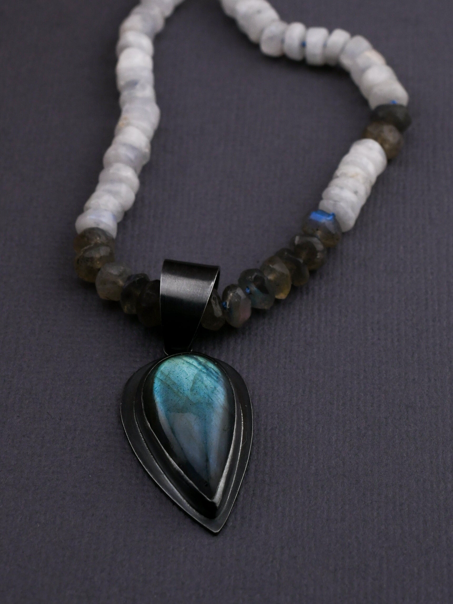 Necklace with a black pendant featuring a blue stone on a dark background