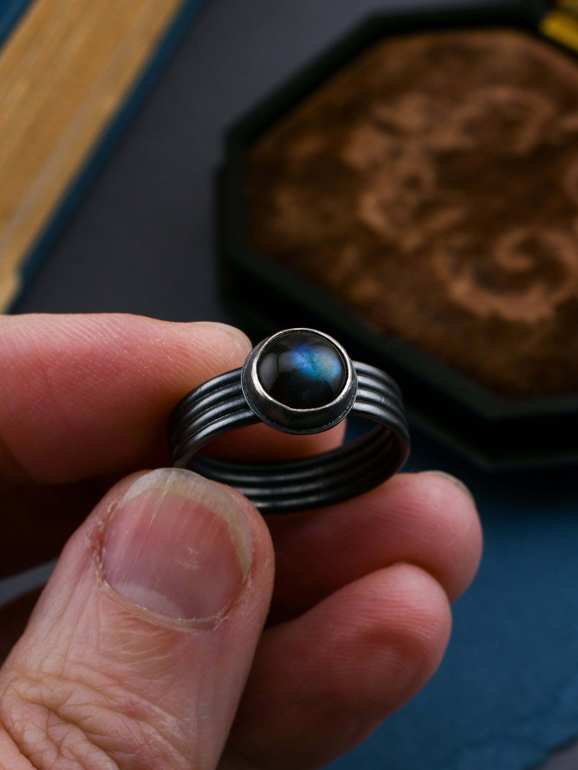 Hand holding a black ring with a central gemstone, blurred background