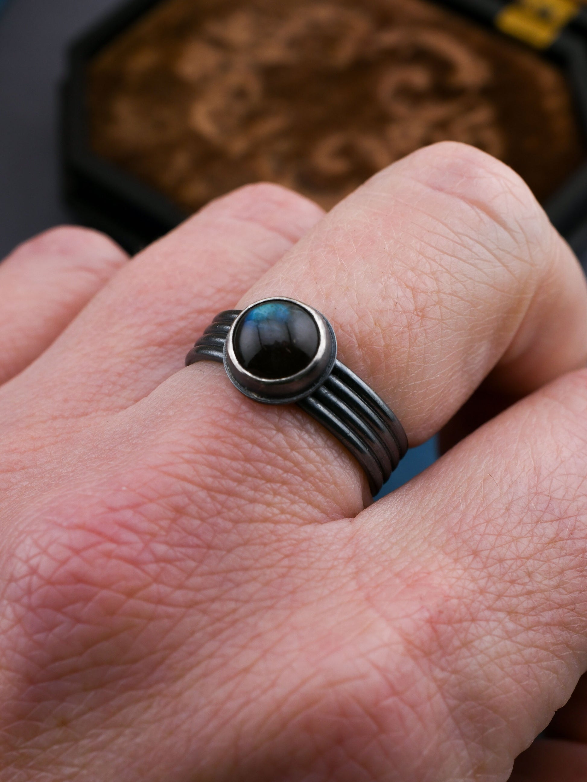 Silver ring with a dark blue gemstone on a person's finger, with a decorative background.
