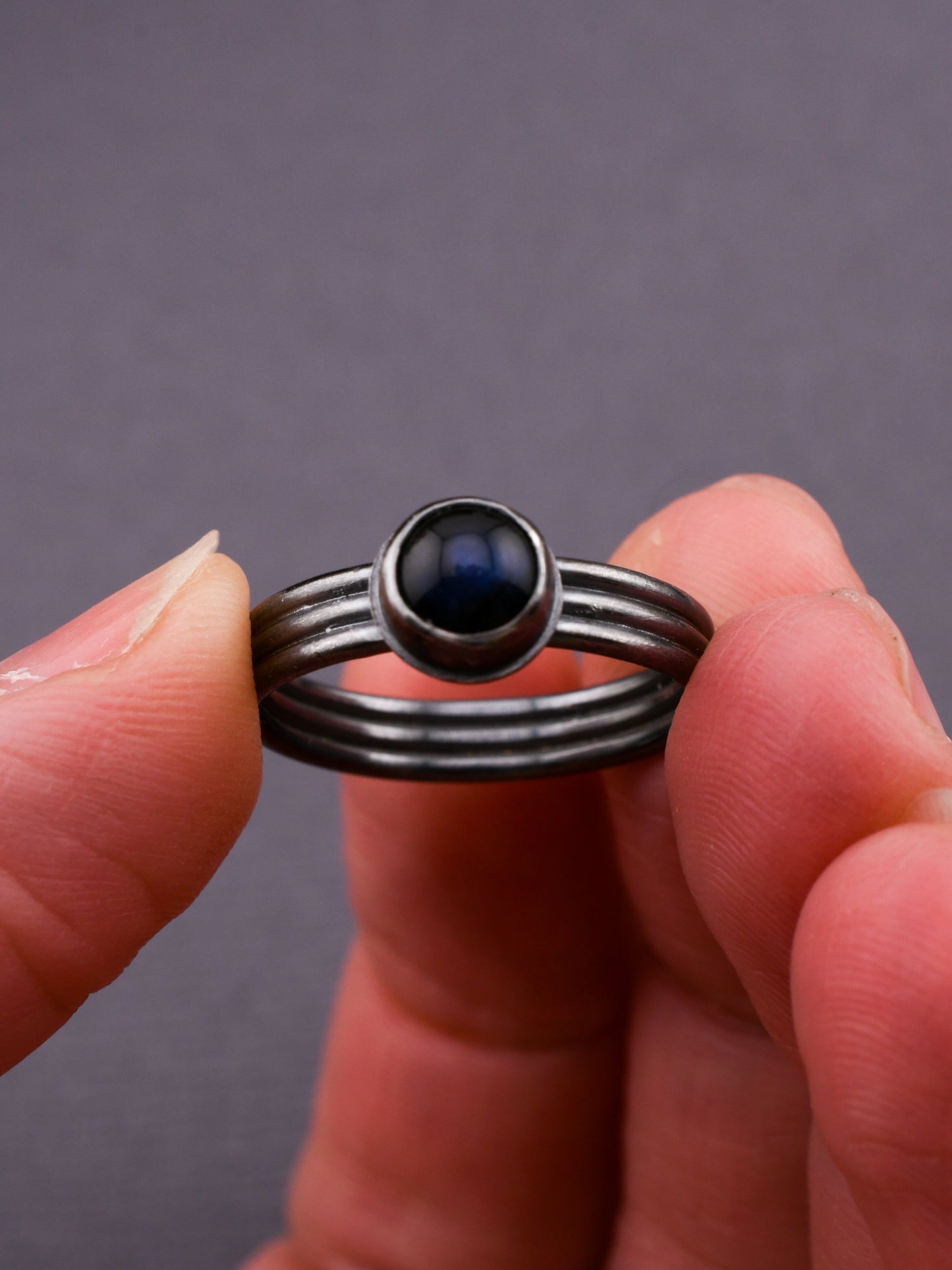 Silver ring with a dark gemstone held between fingers against a gray background