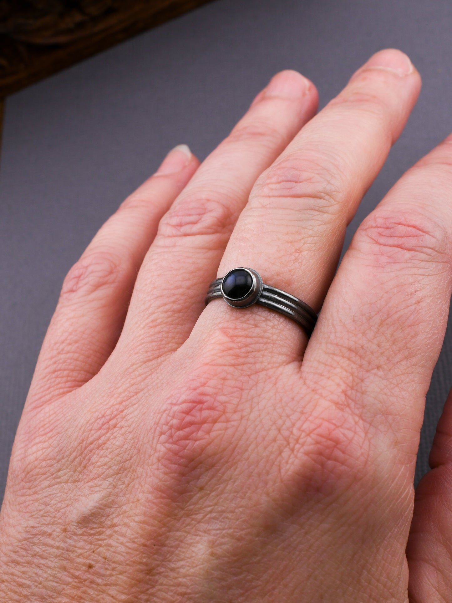Hand wearing a silver ring with a dark blue stone on a dark background