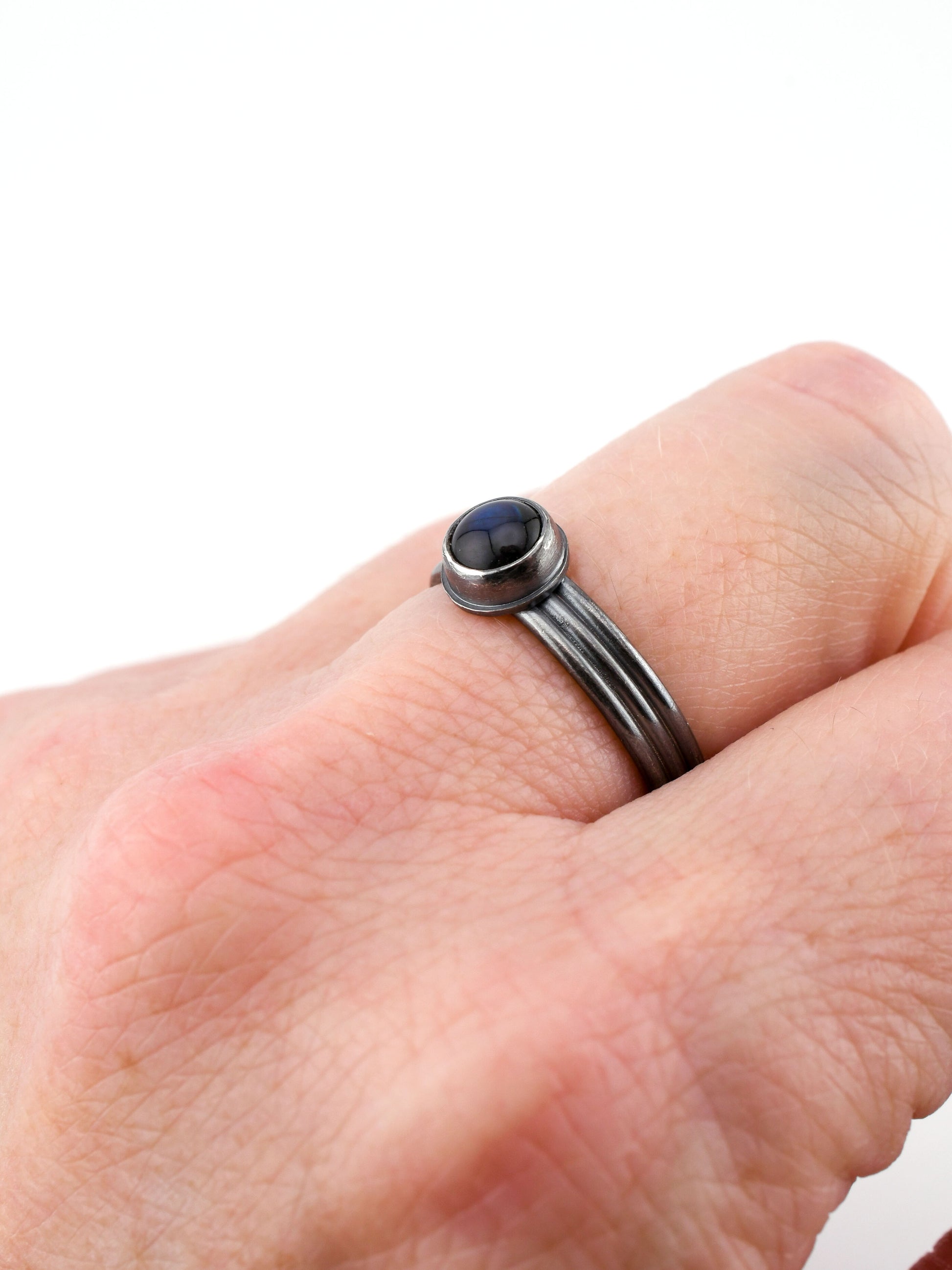 Black ring with a blue stone on a finger against a white background